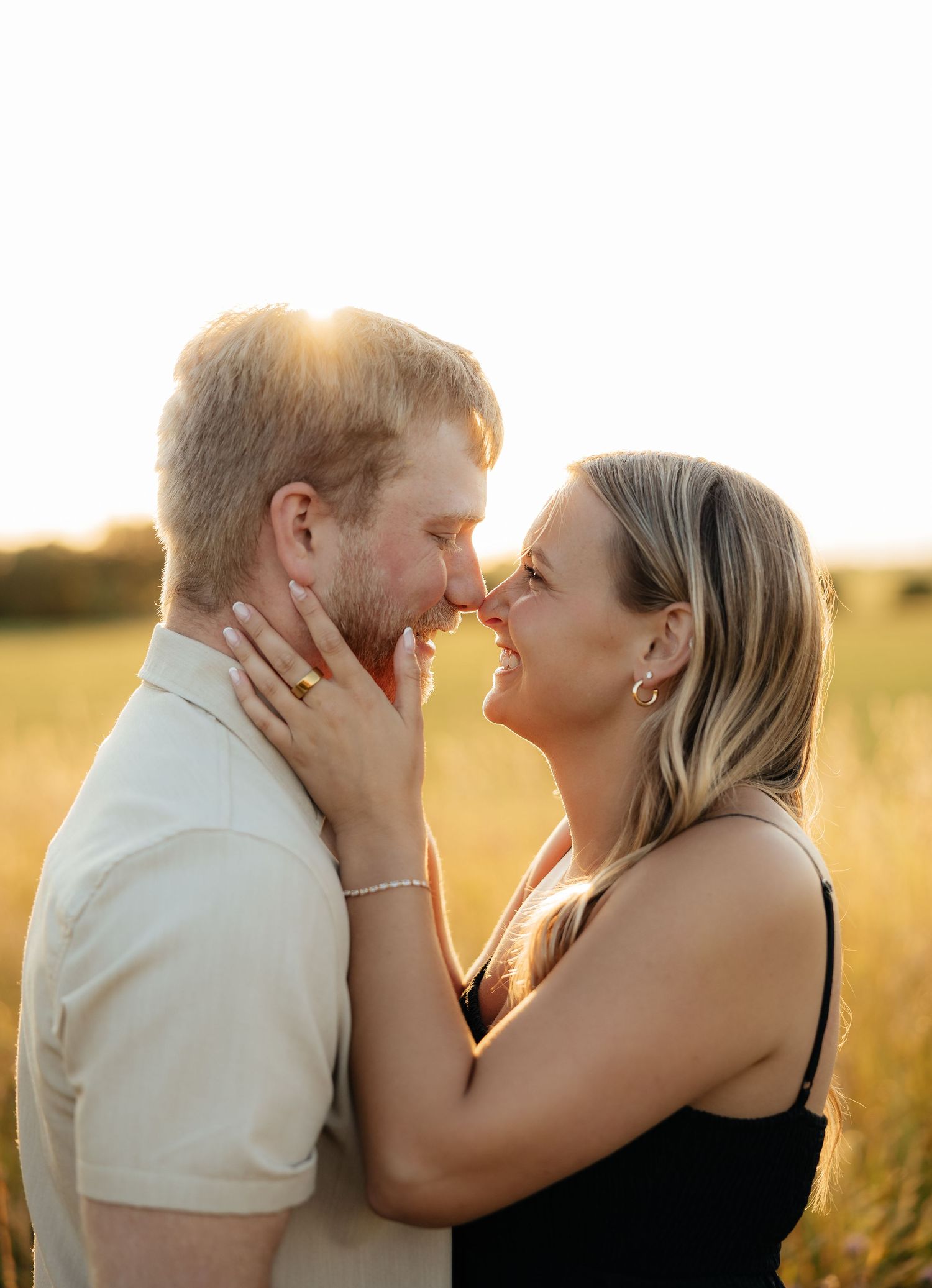 Couple sharing a romantic moment at golden hour in a sunlit field, smiling and touching foreheads.