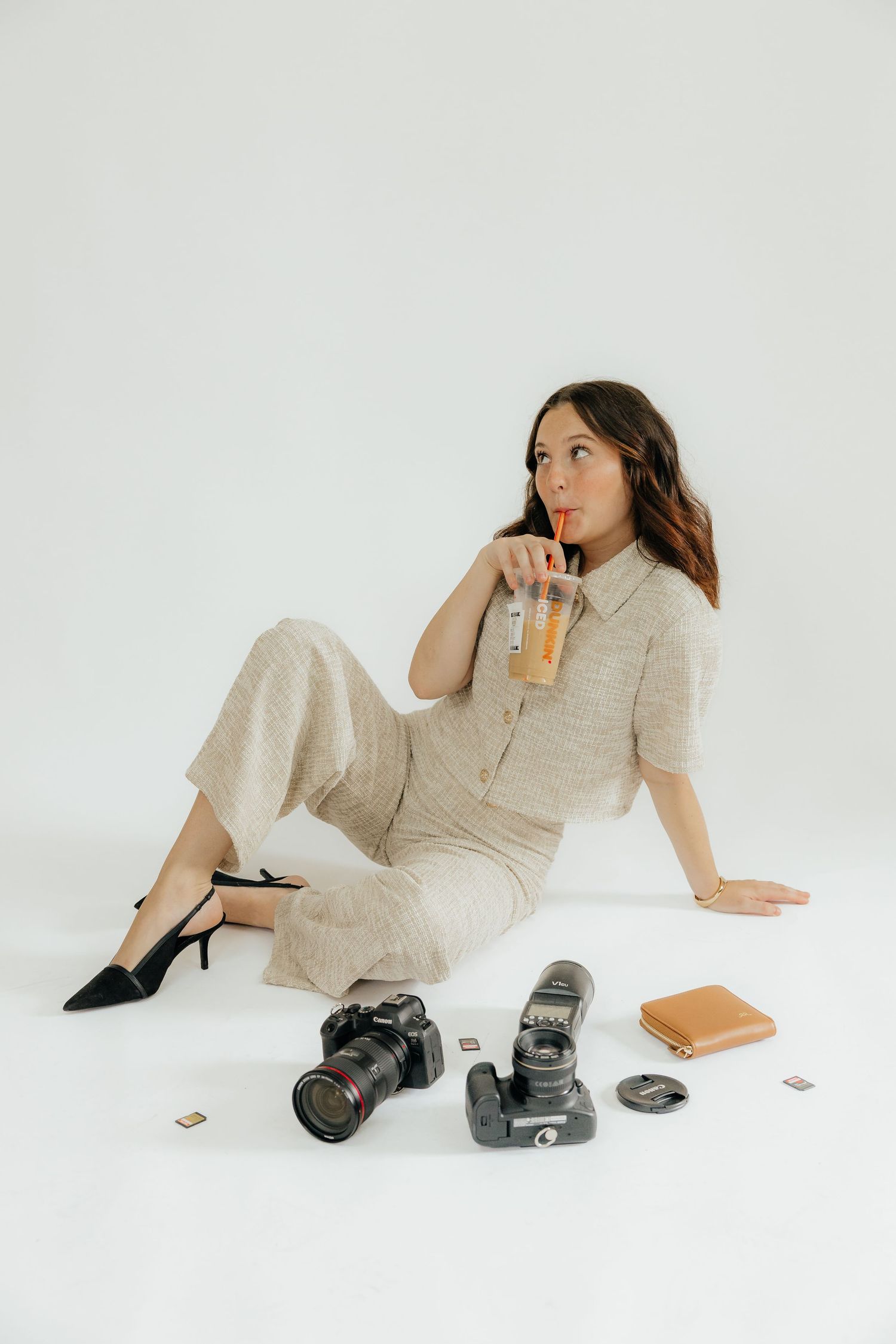 Woman in beige outfit lying on white floor with camera and photography equipment.