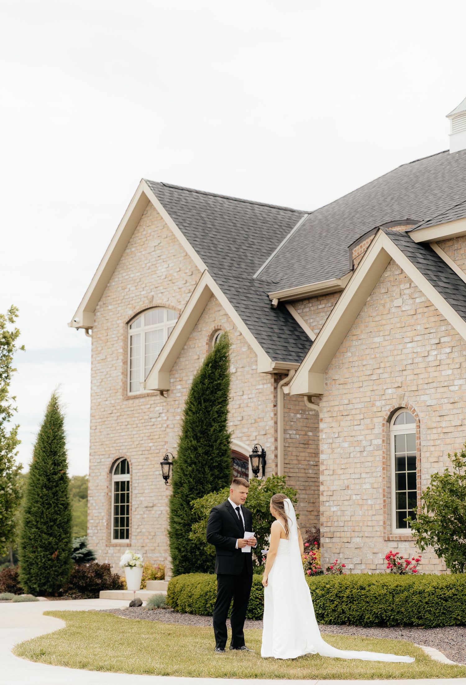 Bride and groom share a first look outside an elegant brick wedding venue surrounded by lush greenery.