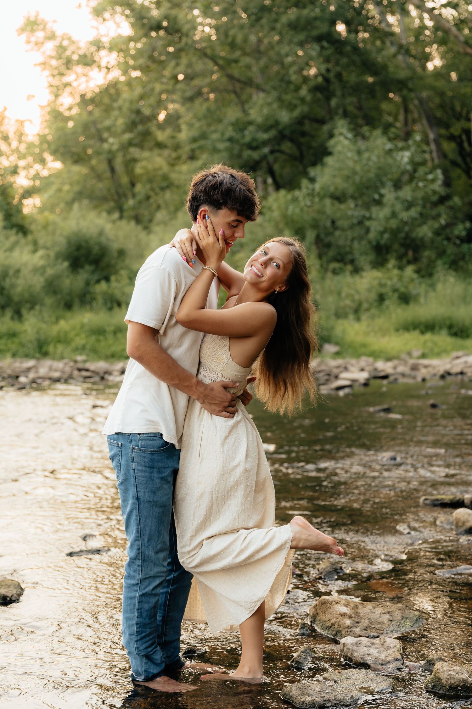 A romantic couple embraces by a rocky riverbank during a golden sunset photoshoot.