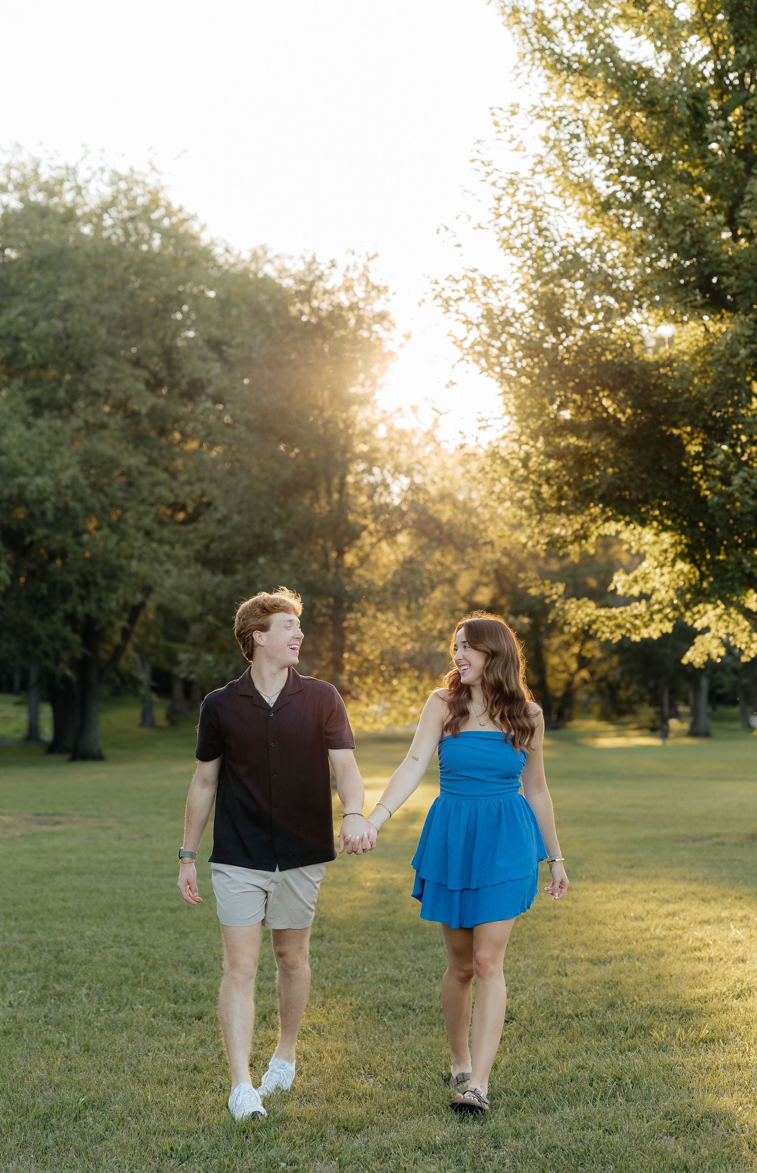 A couple walks hand in hand through a sunlit park at golden hour as warm sunbeams filter through the trees.