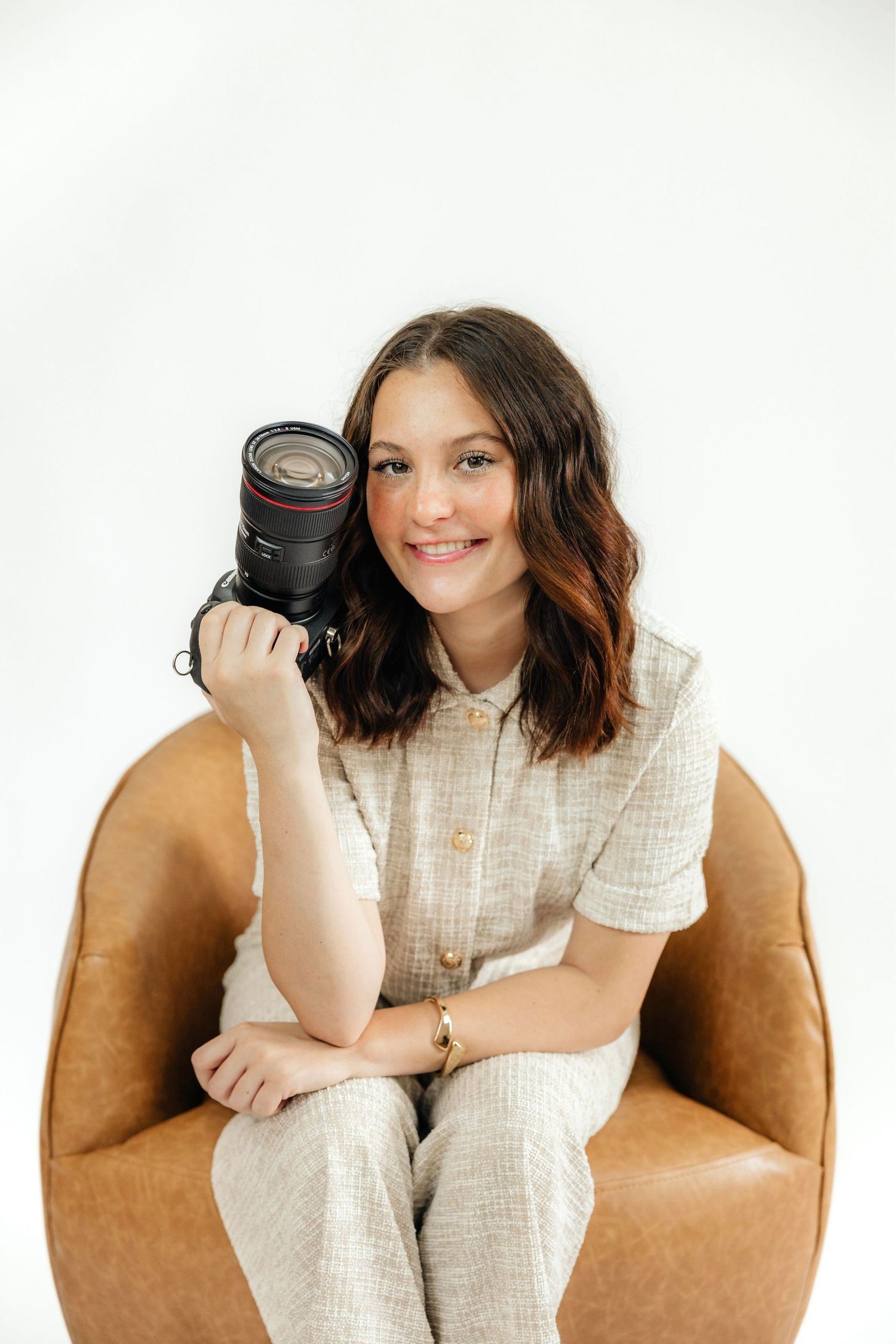 Professional photography series showing a camera lens and casual white outfit against a brown leather chair backdrop.