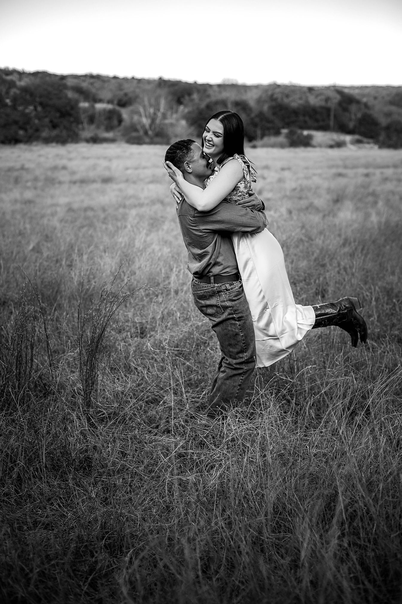 Black and white photo of a groom lifting his smiling bride in a romantic embrace in an open field.