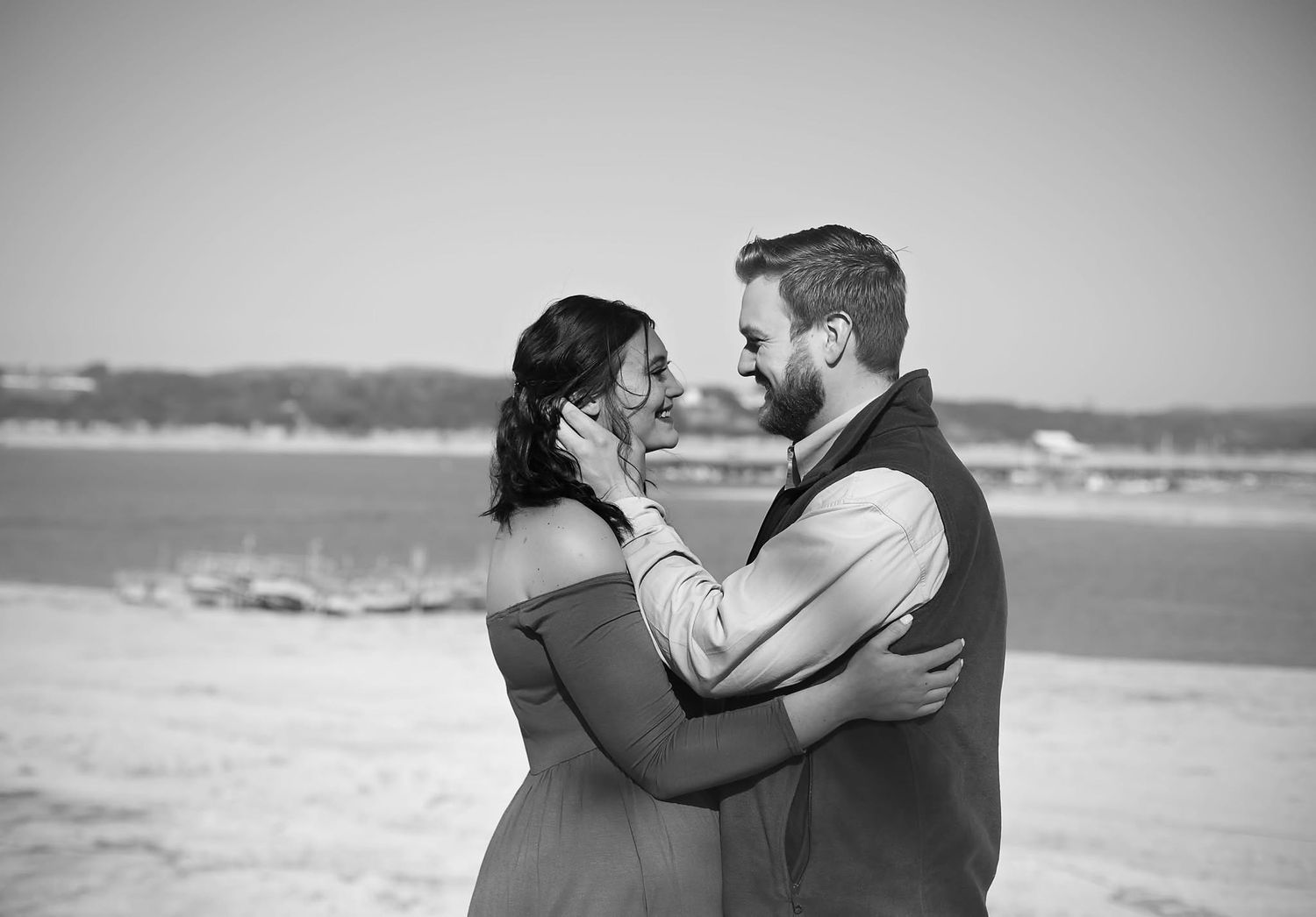 Black and white photo of a romantic couple embracing on a beach, the man tenderly holding the woman's face.