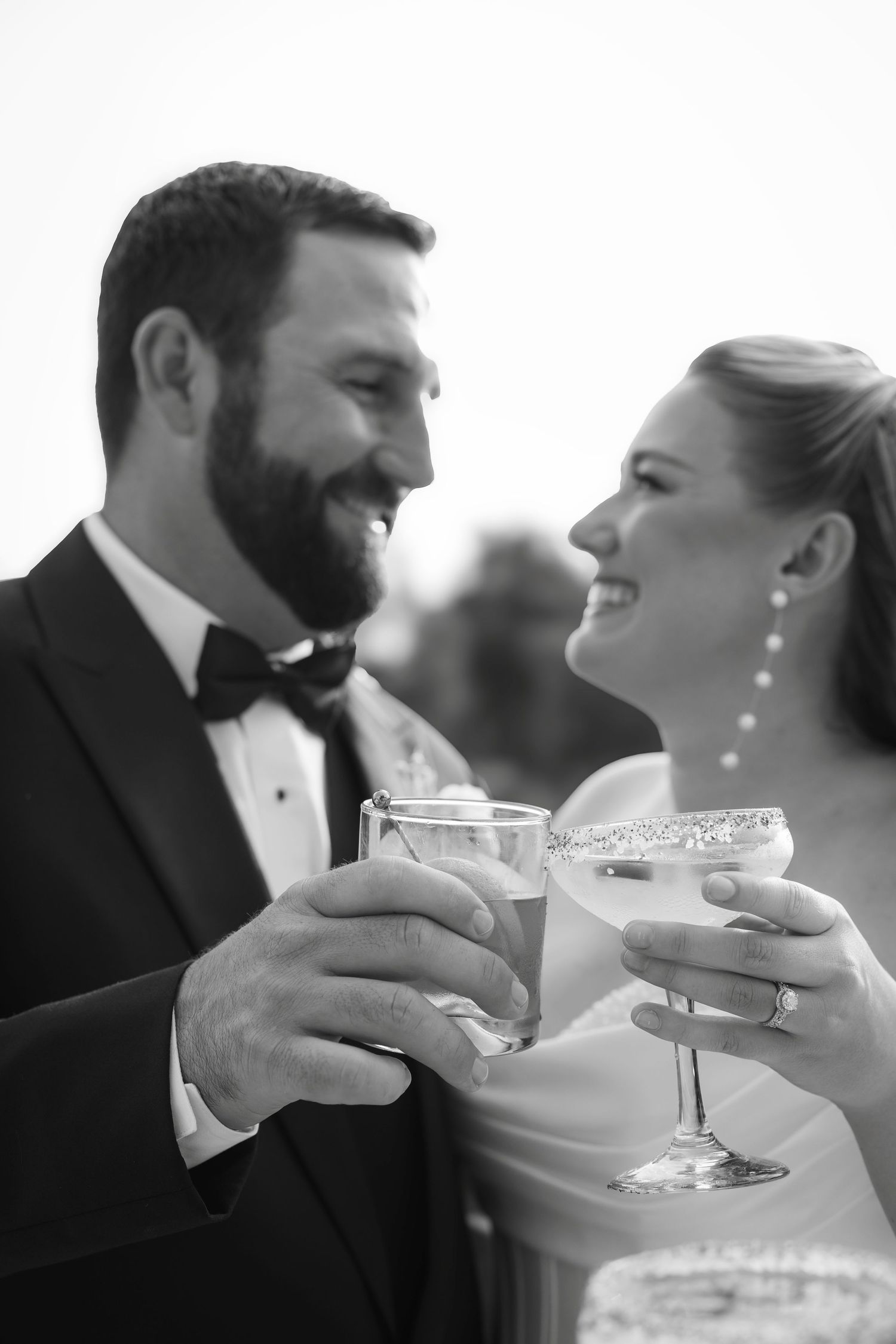 Black and white photo of smiling bride and groom toasting with cocktails at their wedding reception.