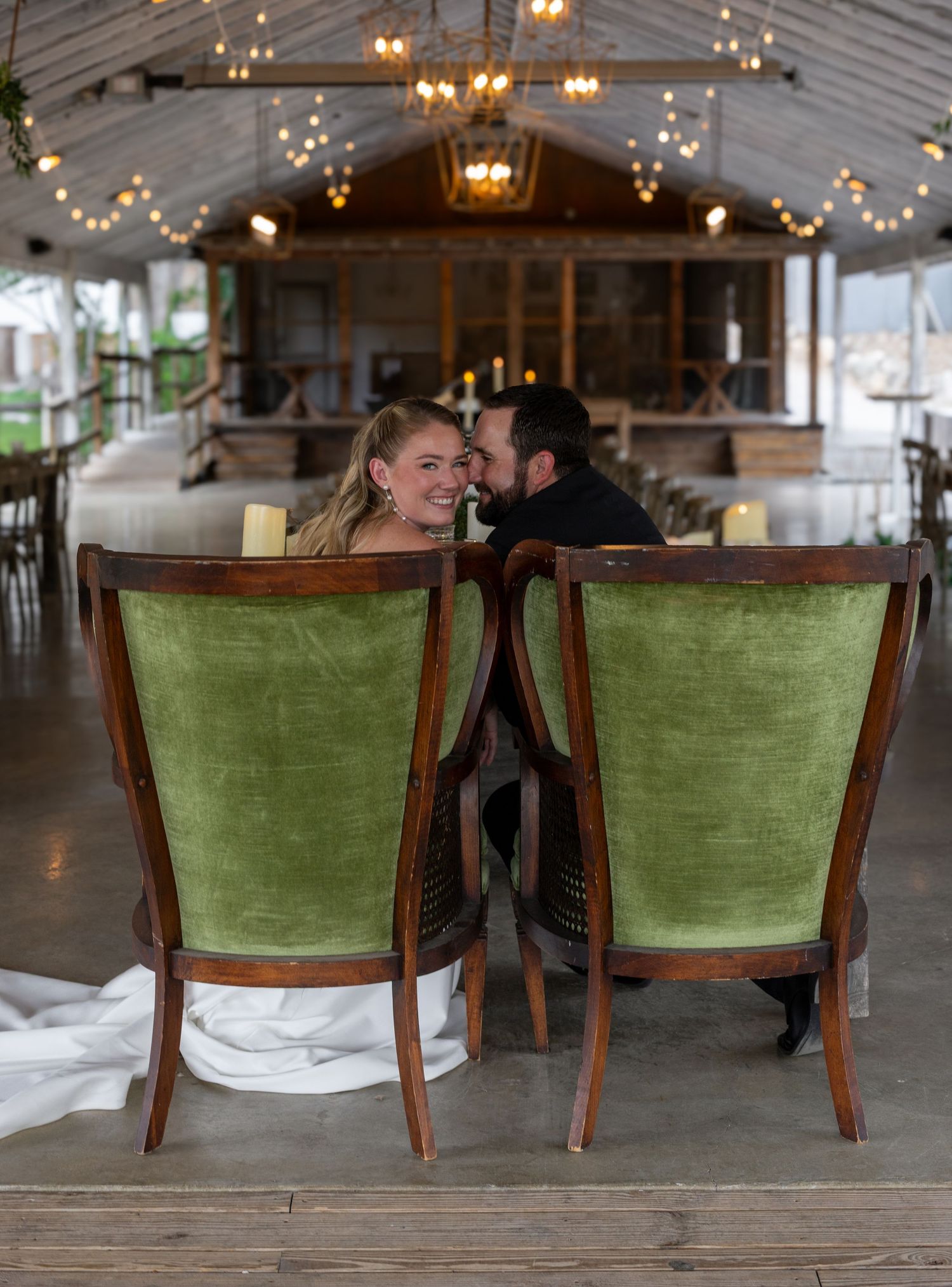 A bride and groom share an intimate moment seated in green velvet chairs at their elegant wedding reception venue.