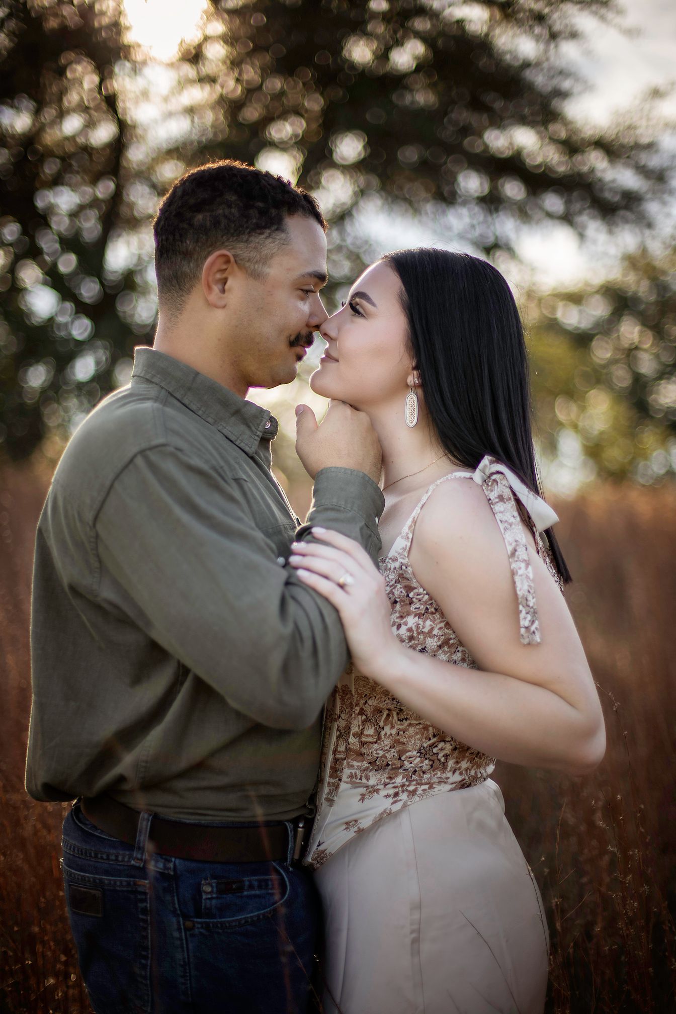 A couple shares a romantic almost-kiss moment in a golden field, the woman in a floral dress and man in a green shirt.
