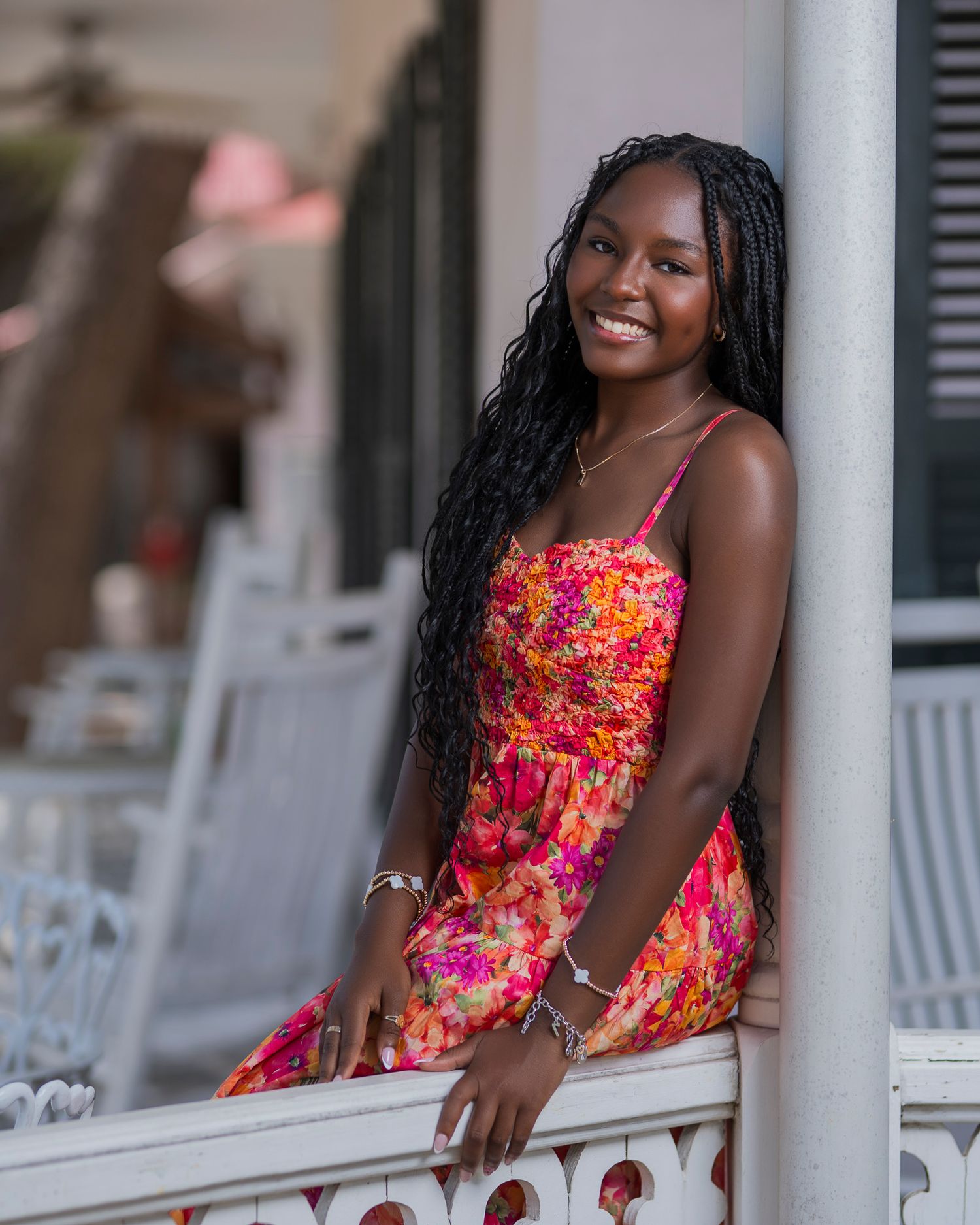 Person in colorful floral sundress smiling while posing on decorative white porch.