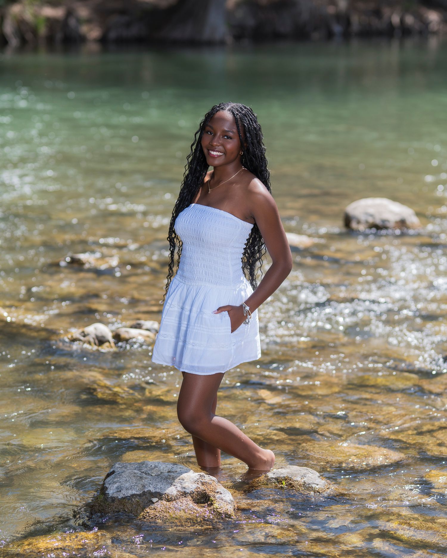 Casual summer portrait in white dress standing in shallow stream water.