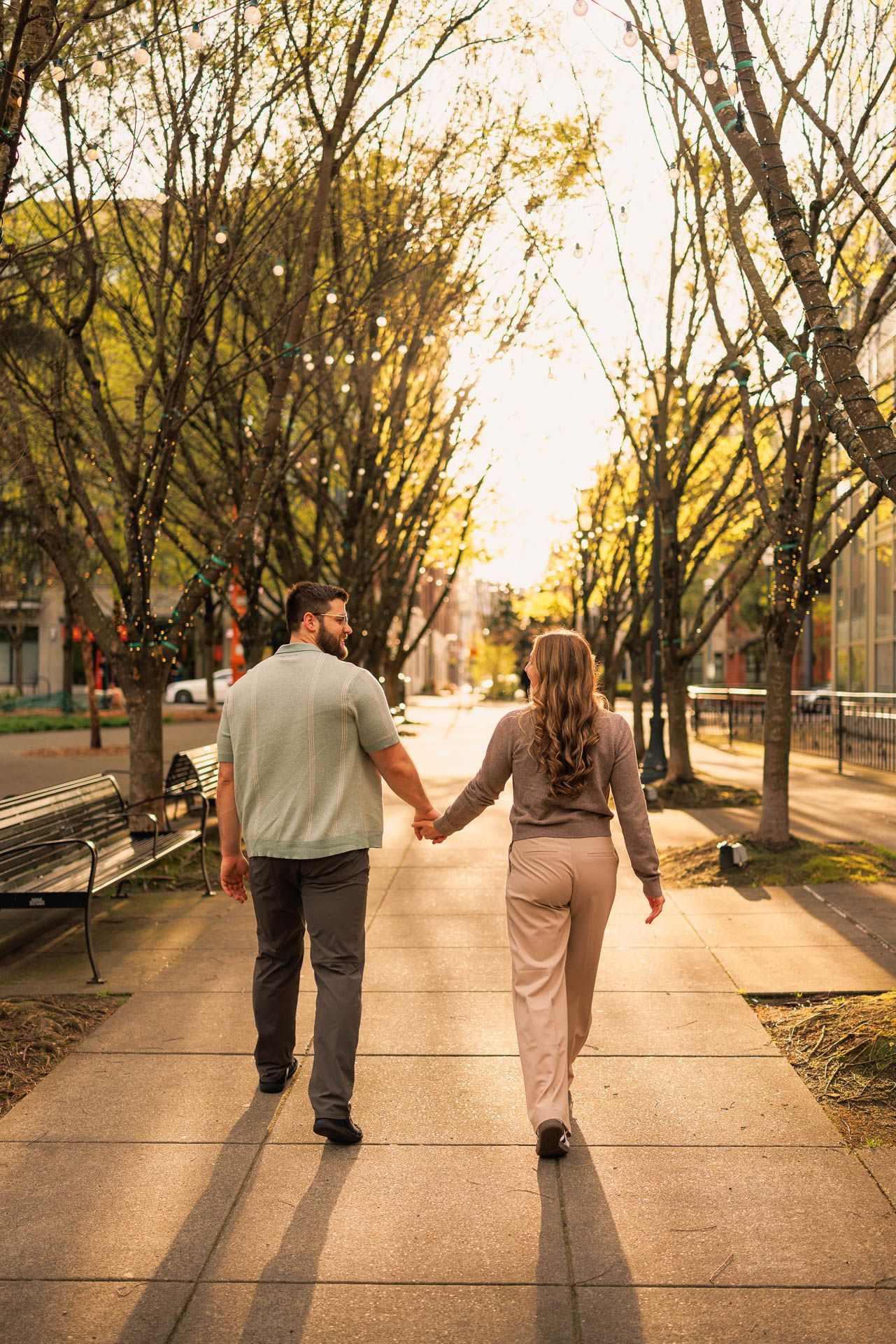 Couple strolls hand in hand down tree-lined path during golden hour.