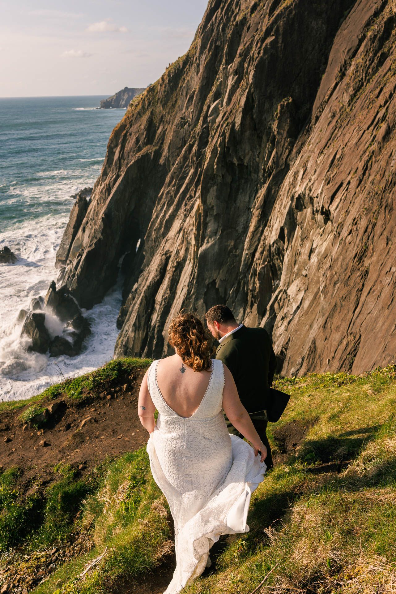 Couple walking along dramatic coastal cliffs with crashing waves below.