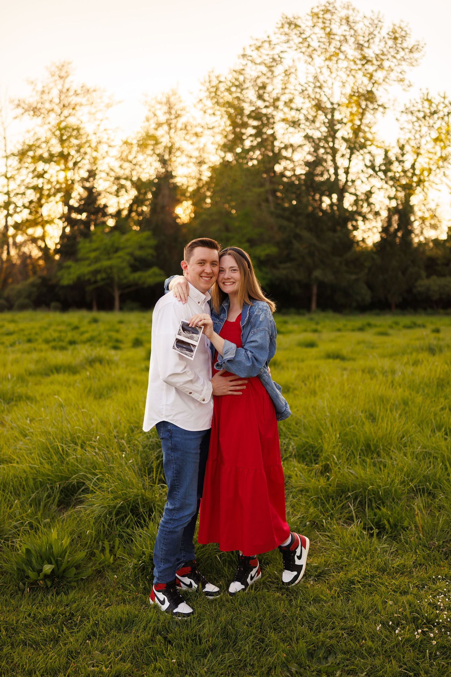A couple embraces in a grassy field at sunset wearing matching Nike shoes and casual attire.