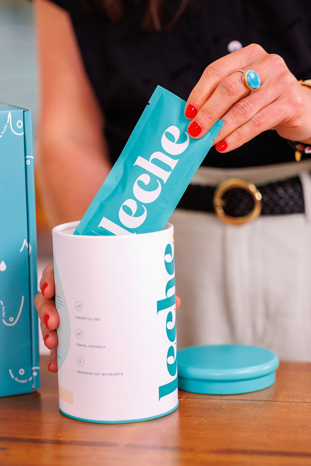 A sequence of hands placing small teal-colored boxes into larger white storage containers on a wooden surface.