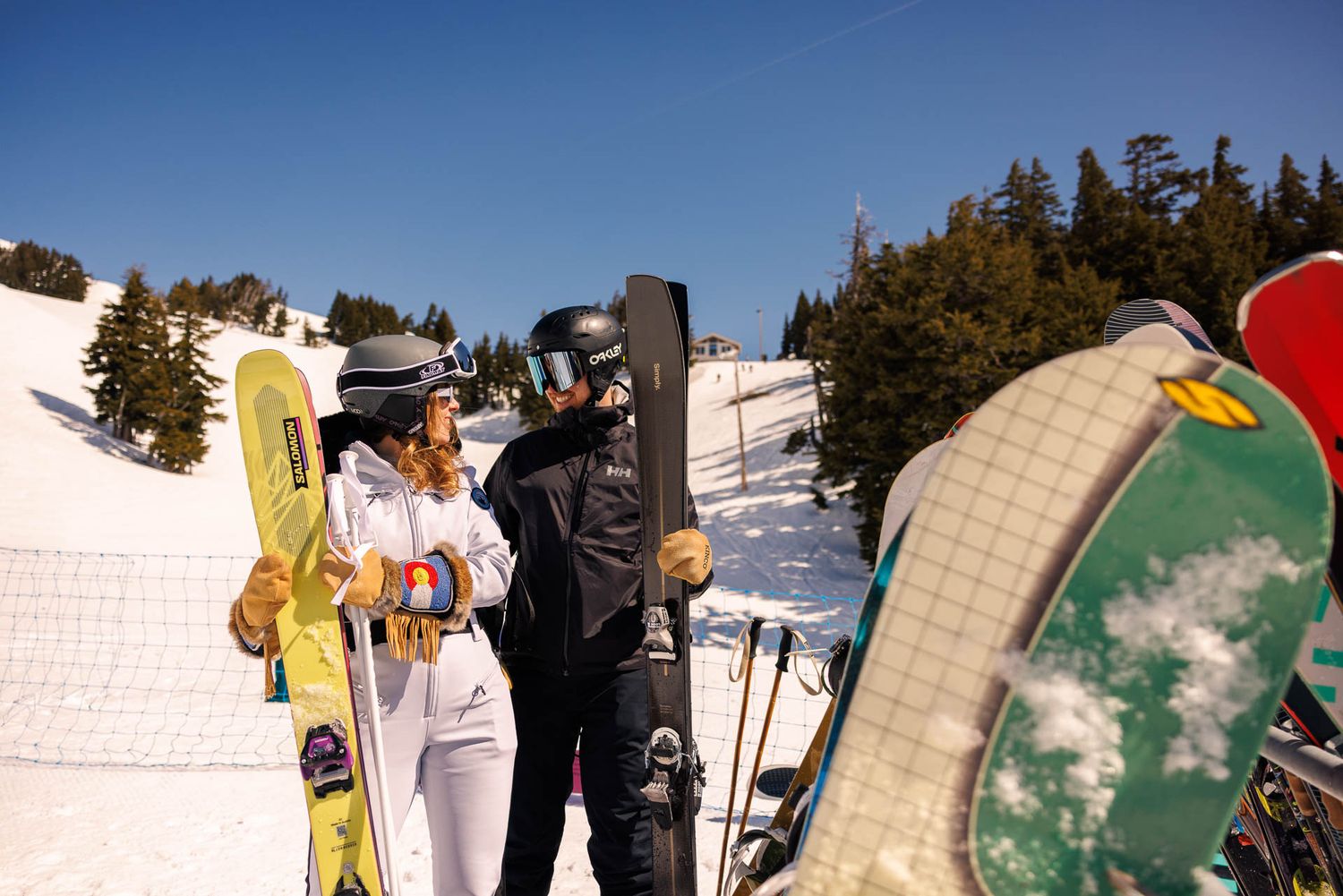 Skiers taking a break at the top of a sunny mountain slope with equipment.