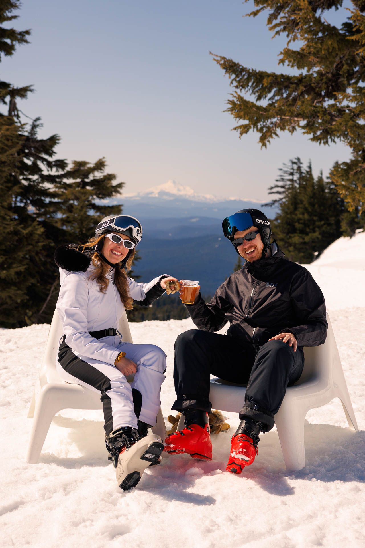 Two snowboarders relaxing and enjoying a break in snow chairs with mountain views in the background.