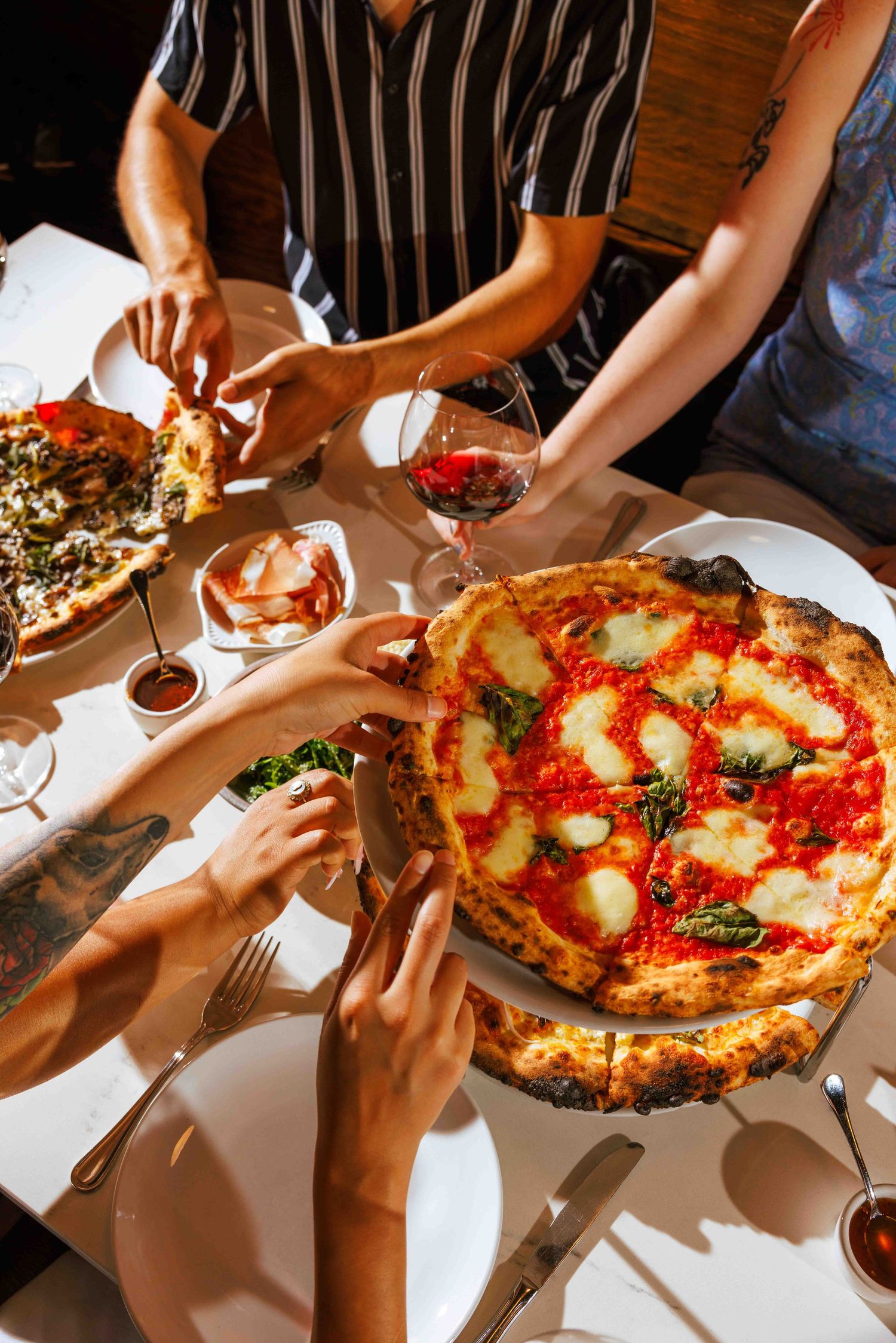Friends sharing authentic Neapolitan pizza and wine at restaurant table with classic Margherita pizza in focus.