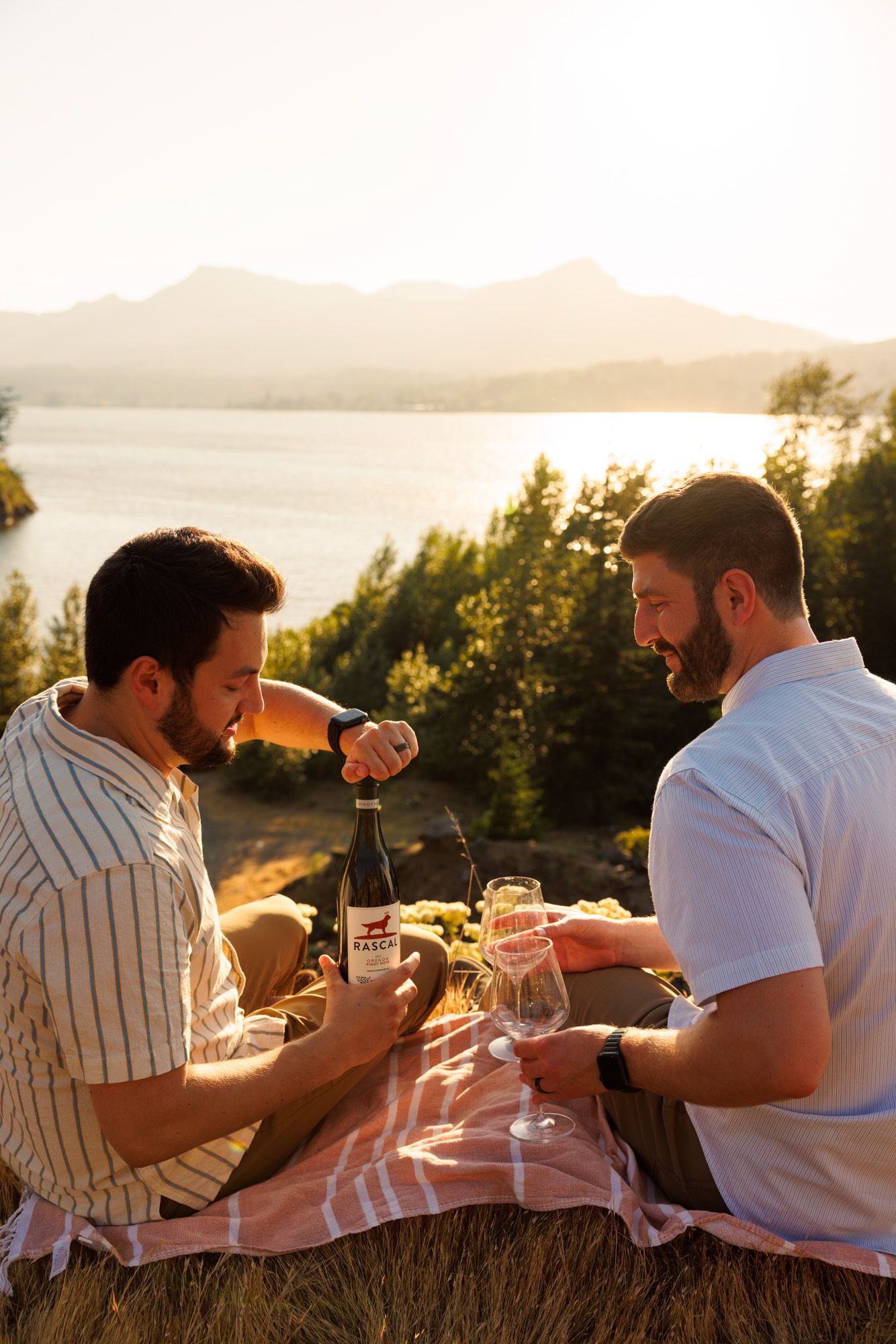 Two friends share wine and conversation while enjoying a scenic golden hour picnic in nature at sunset.