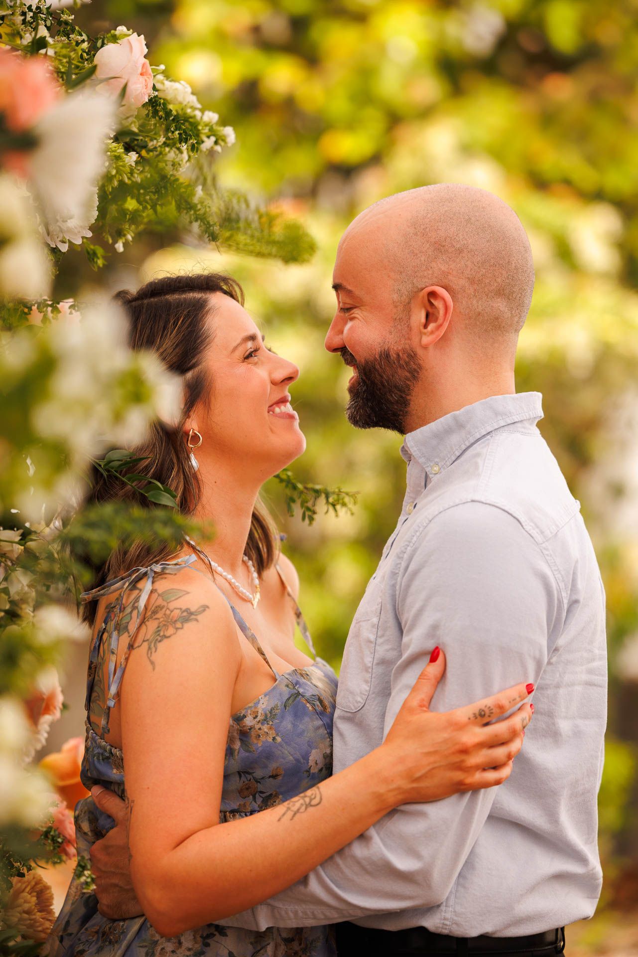 A romantic couple embraces outdoors among blooming spring flowers with soft natural lighting and bokeh effect.