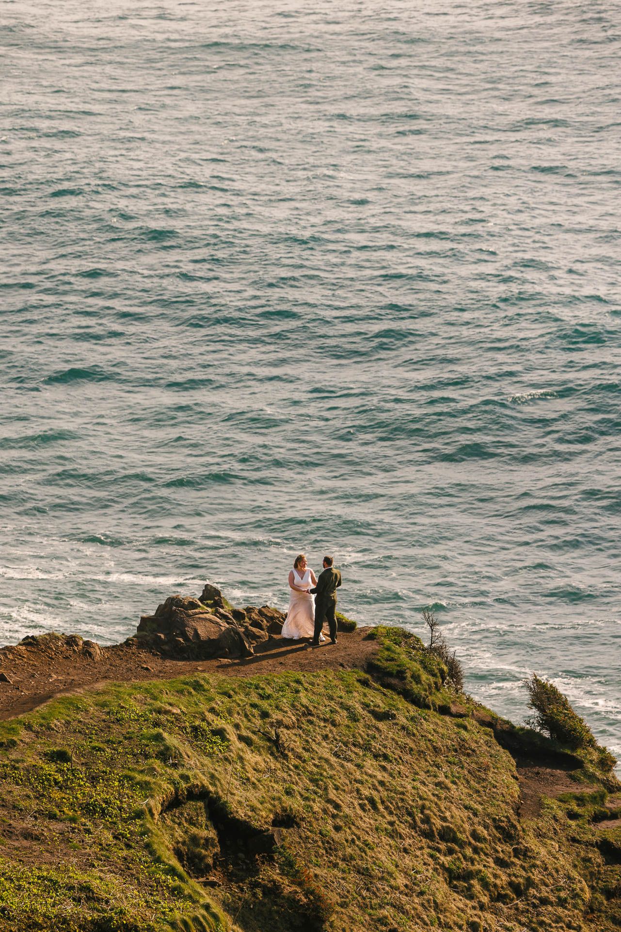 A coastal hillside scene showing figures gazing at the expansive ocean view from a grassy cliff edge.