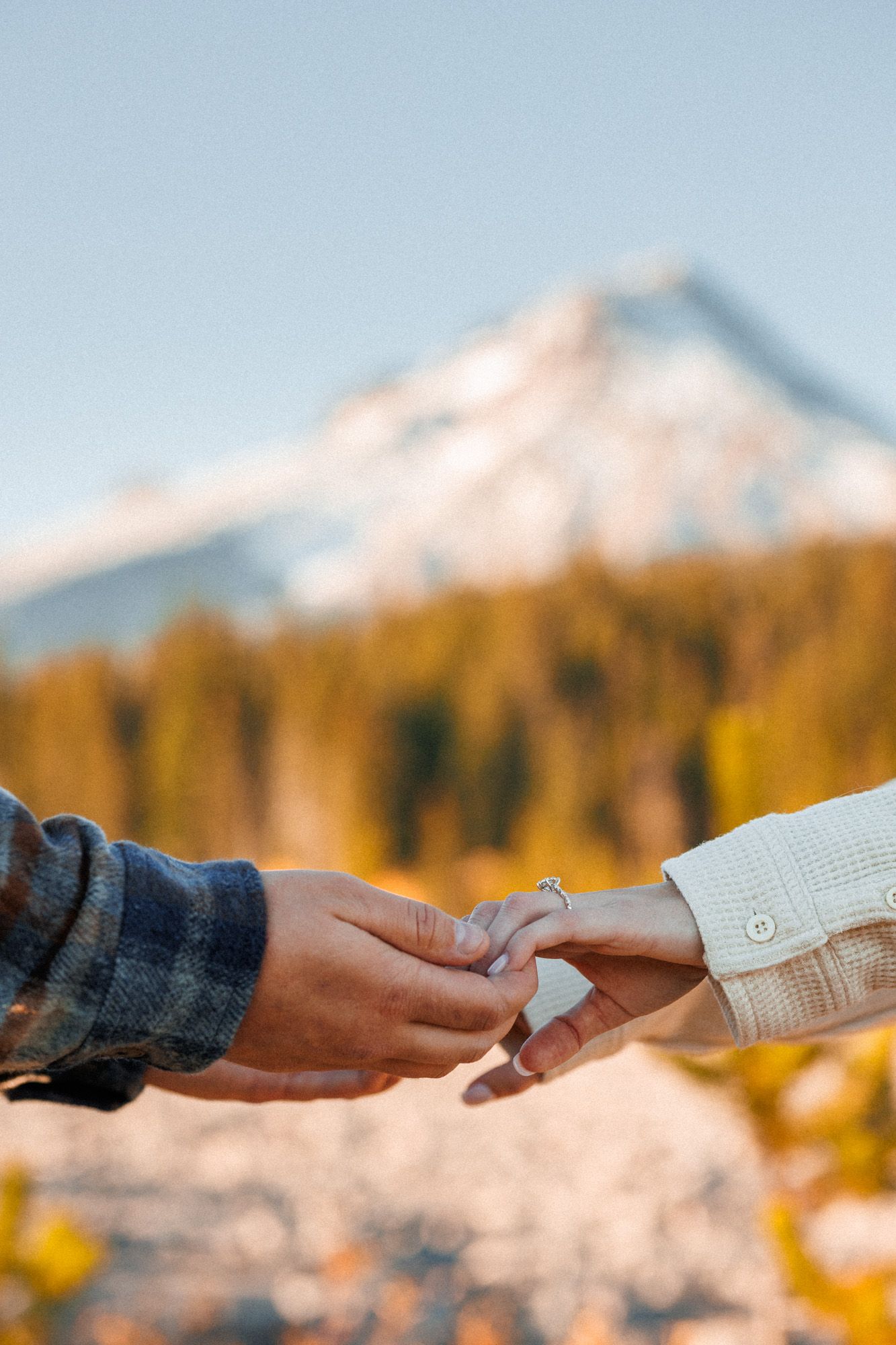 Two hands exchanging currency against a scenic mountain backdrop with autumn trees in the foreground.