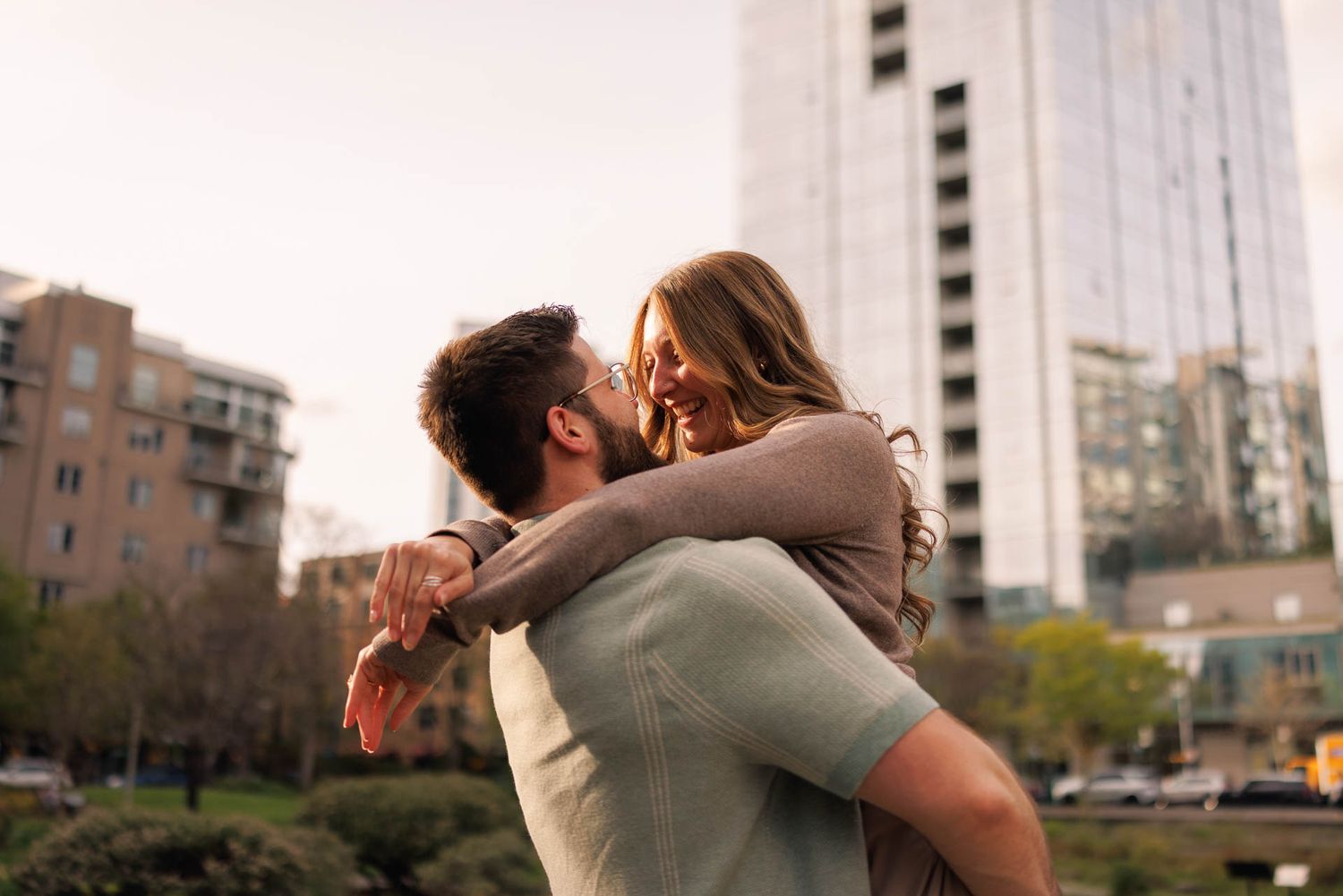 Joyful couple embraces and shares romantic moment in front of urban cityscape at sunset.