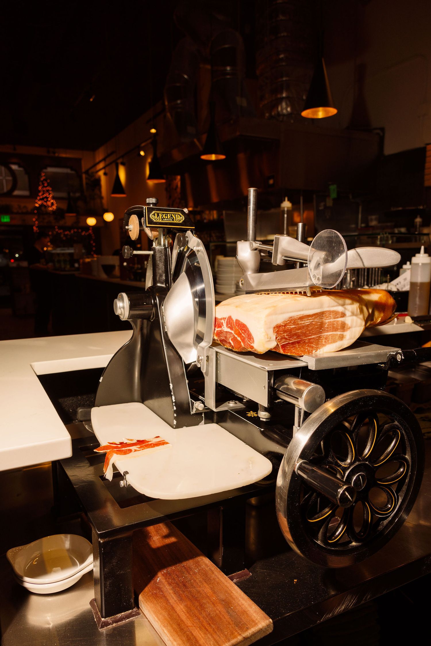 Vintage meat slicers lined up on a dark wooden counter in a dimly lit restaurant or deli setting.