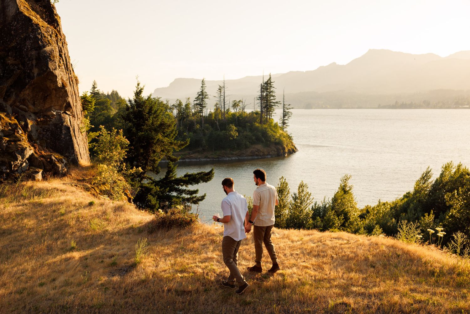 Two people stroll along a scenic coastal trail during golden hour as the sun sets over the calm waters.