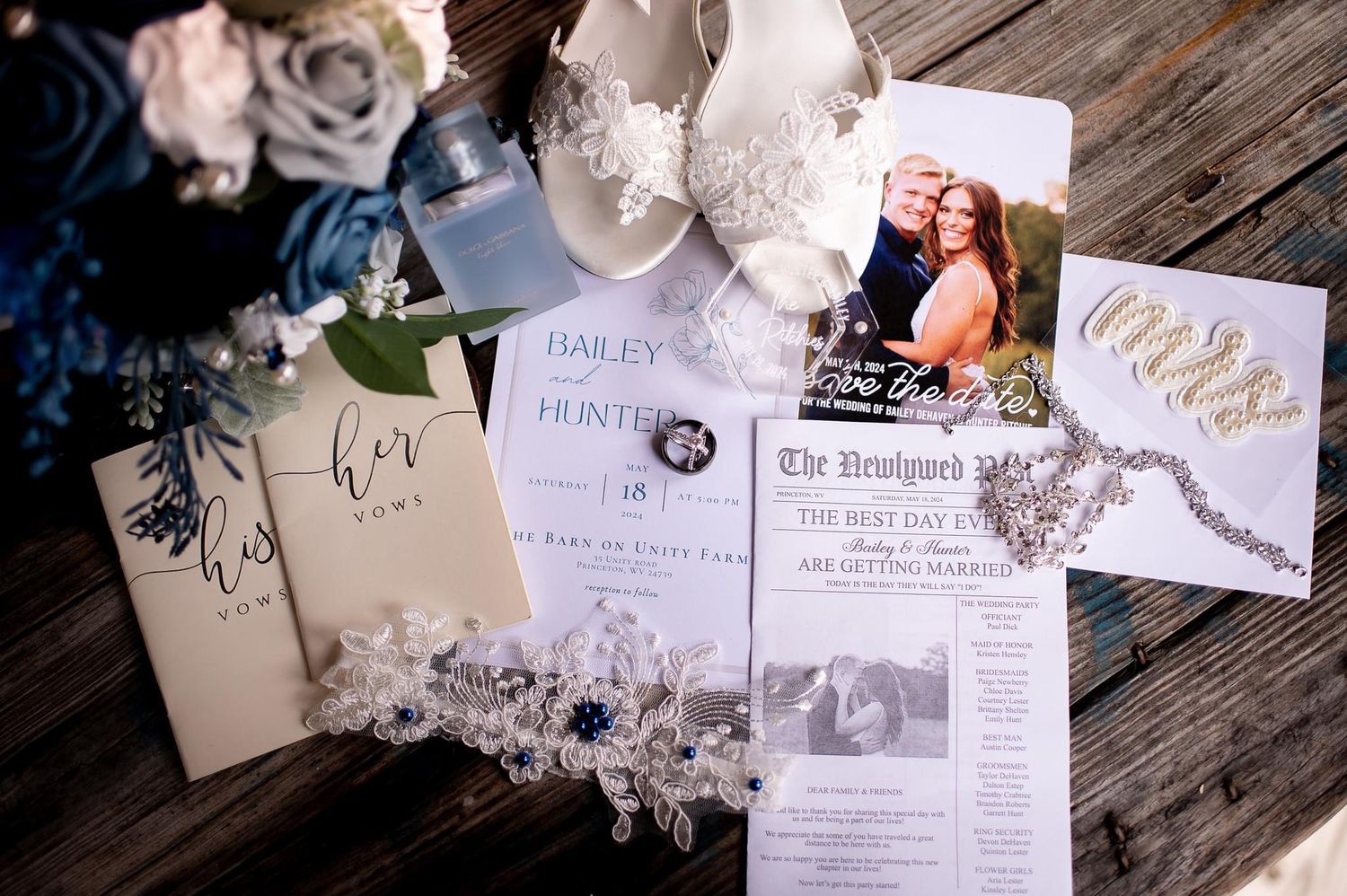 Wedding invitations and details flat lay with roses and lace on rustic wooden surface.