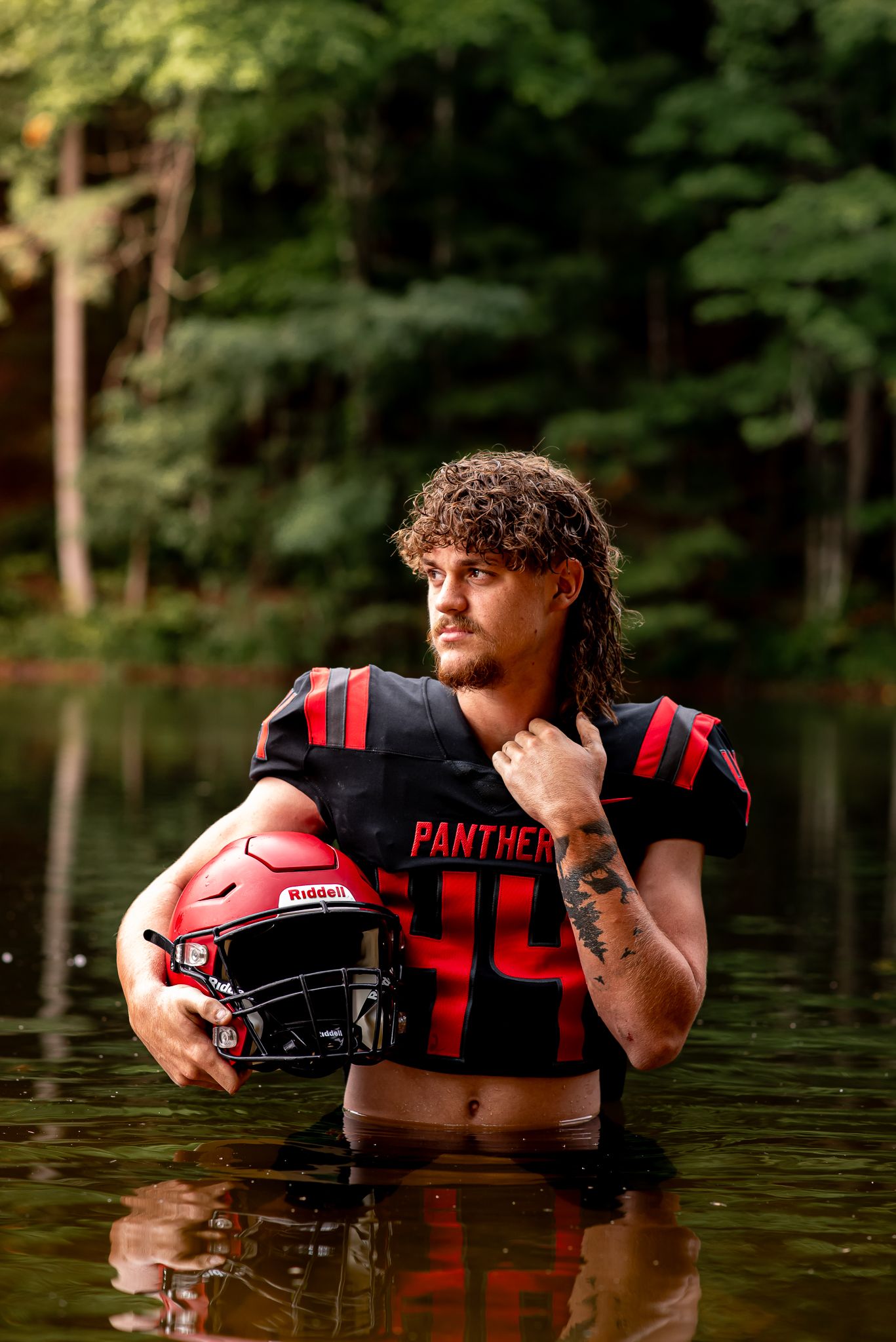 Football player in black and red uniform poses in water for dramatic sports portrait.
