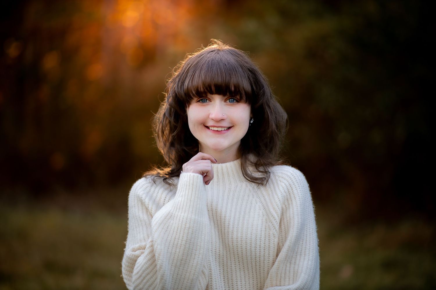 Portrait in white sweater against autumn backdrop with warm lighting.