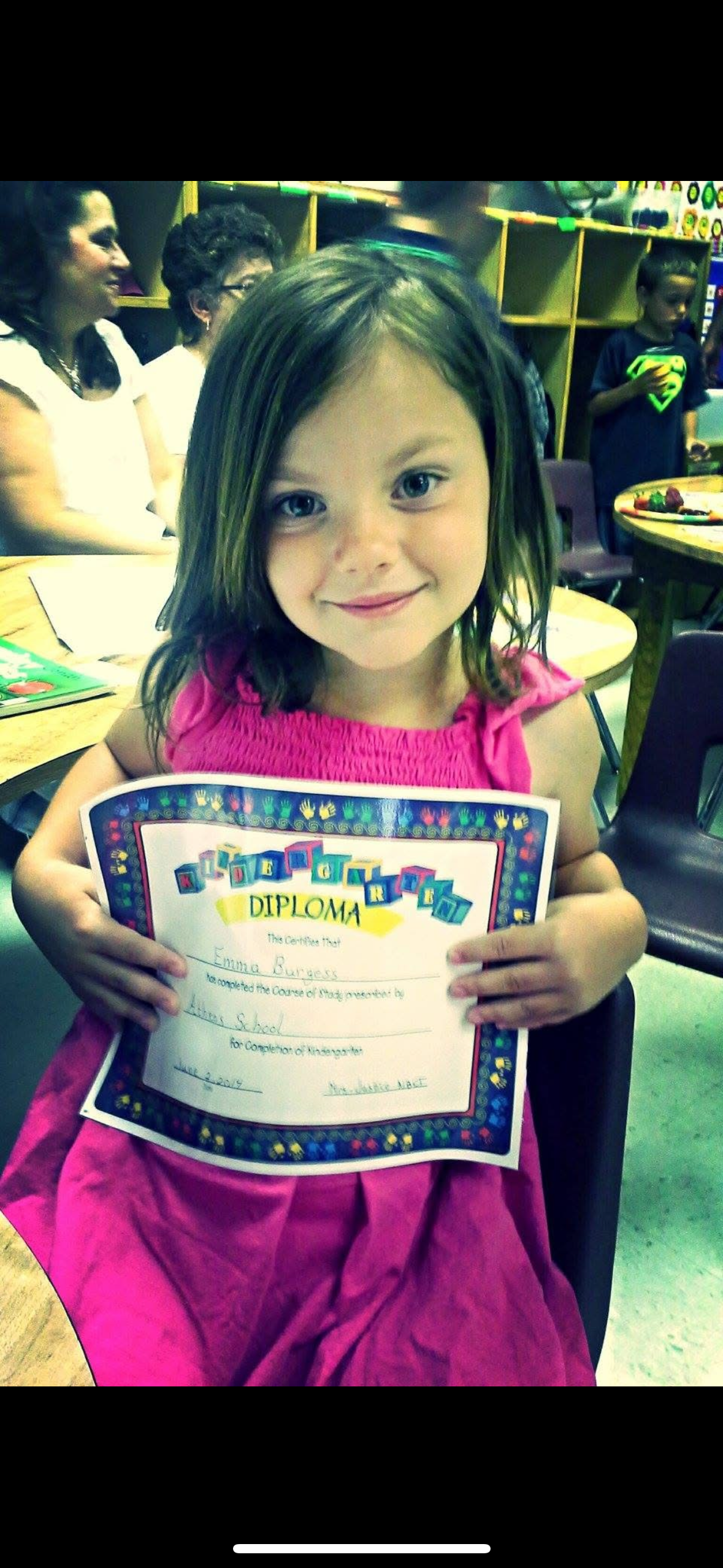 A young student in a pink top proudly displays their school diploma certificate.