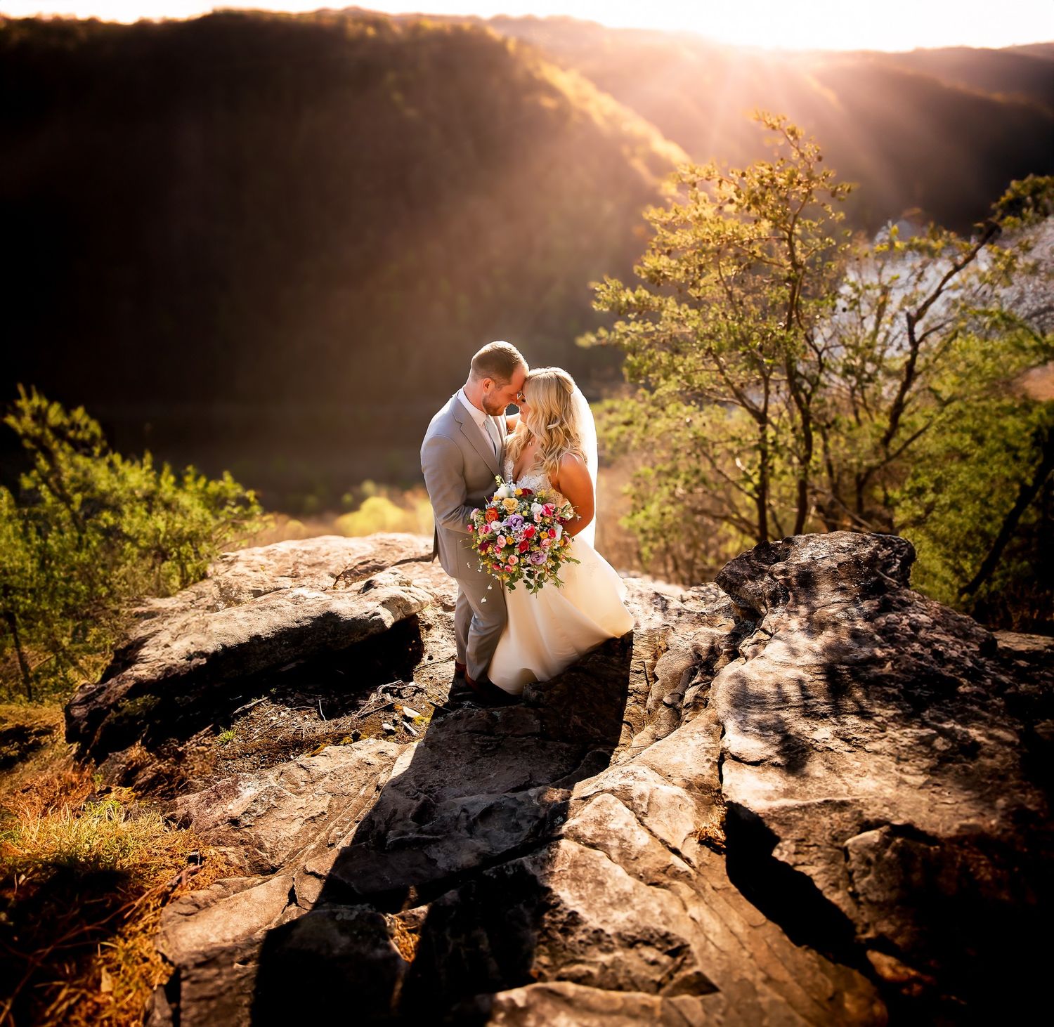 Dramatic sunset wedding portraits captured on rocky mountain ledge with golden light.
