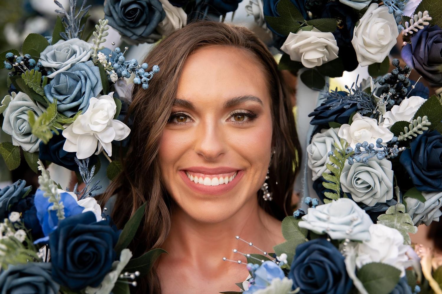 Elegant floral arrangement of blue and white roses frames a joyful wedding portrait against dark background.