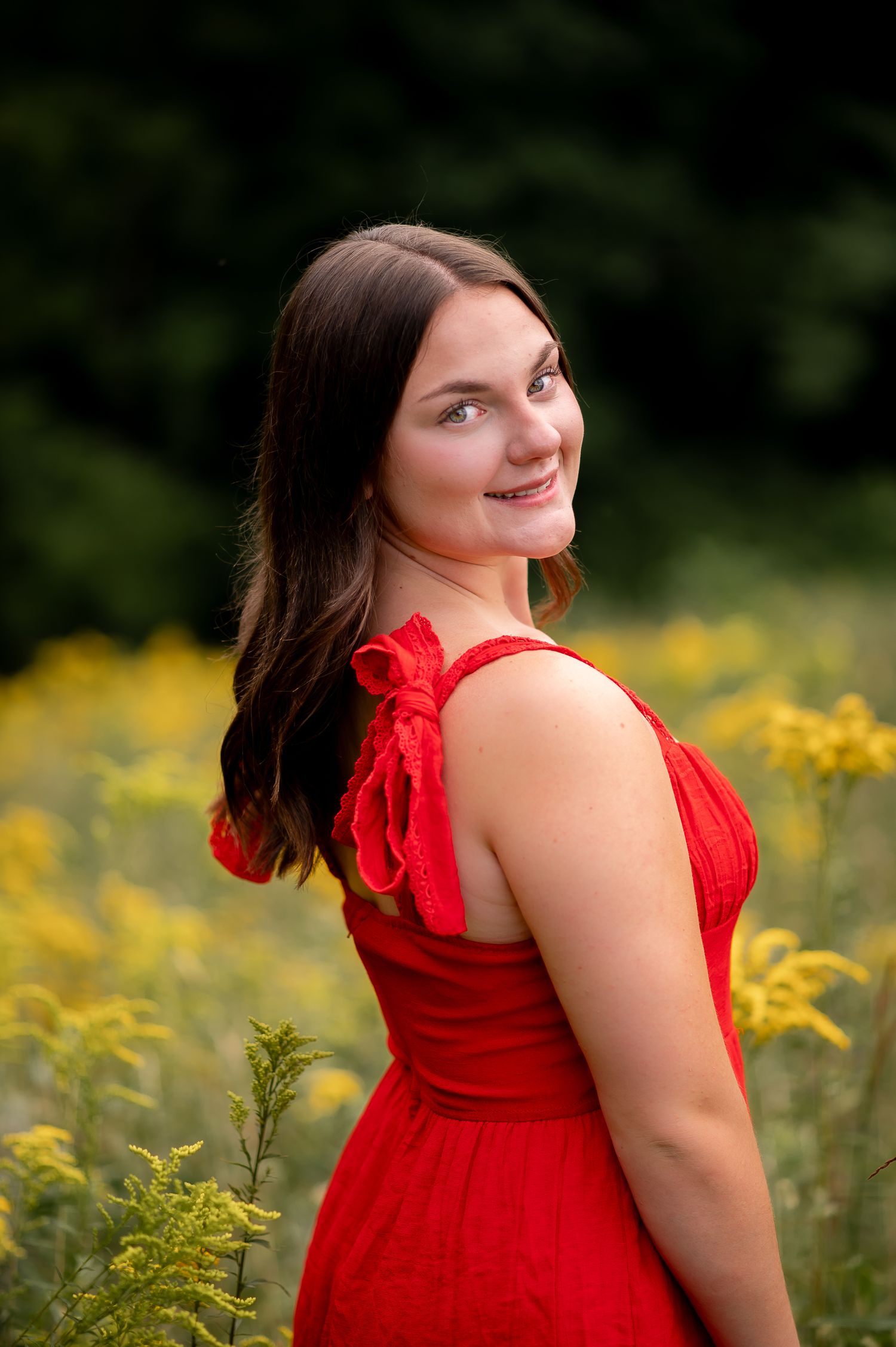 A vibrant outdoor portrait featuring someone in a red sleeveless dress amid blooming yellow wildflowers in a natural setting.