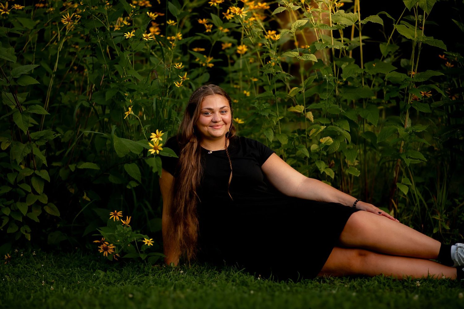 Summer evening portrait laying in garden with black dress among yellow flowers.