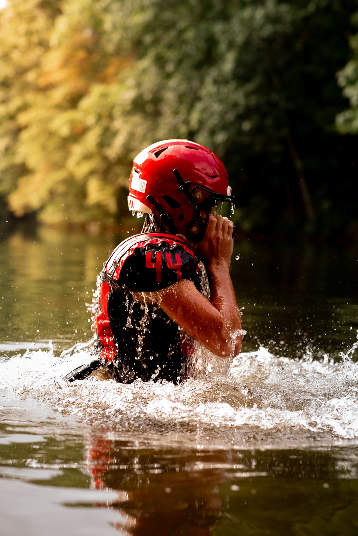 Person in red kayaking helmet and gear emerging from water splash during outdoor water sports activity.