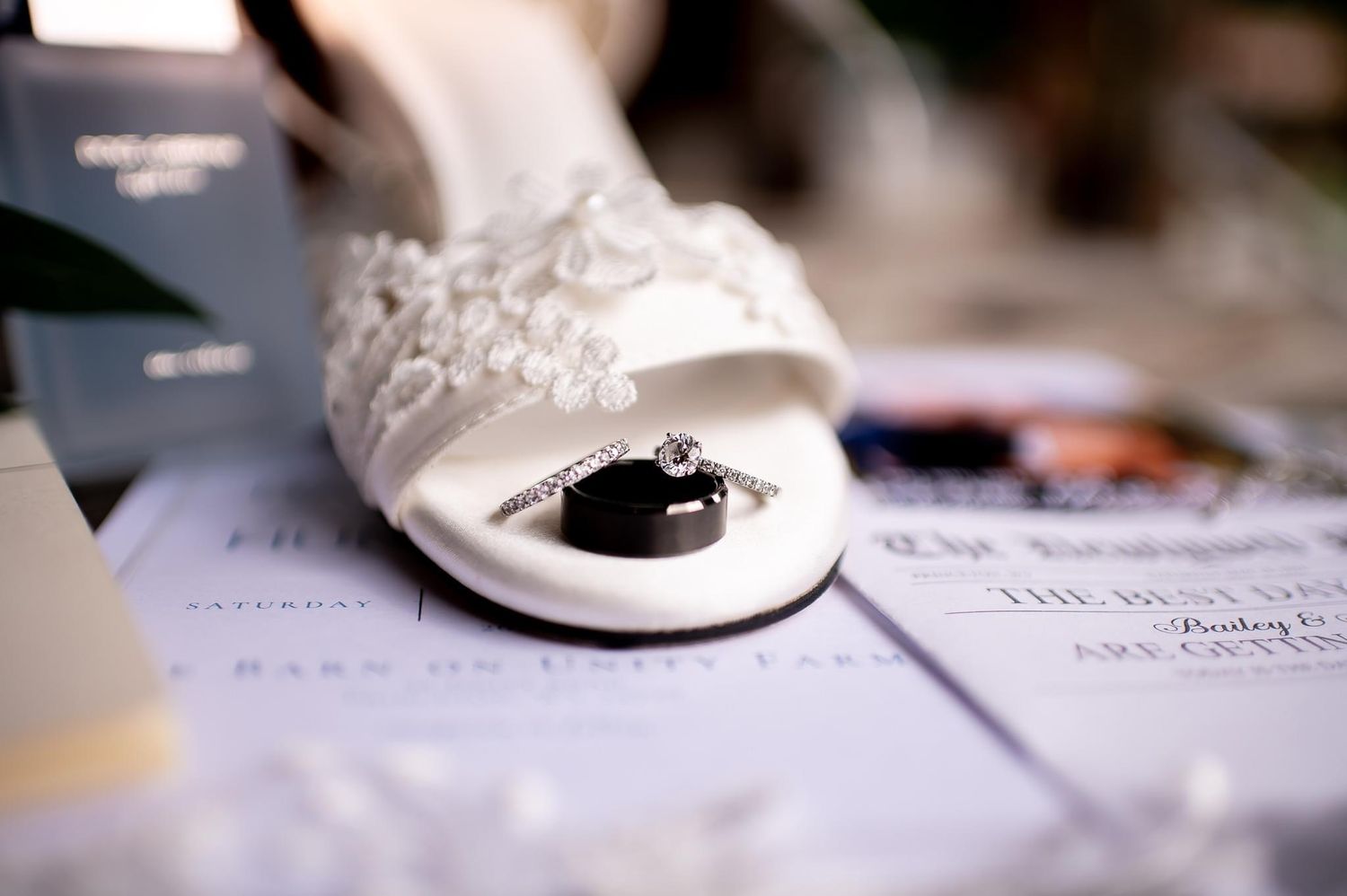 Close-up of elegant white bridal shoe with wedding rings placed on paper.