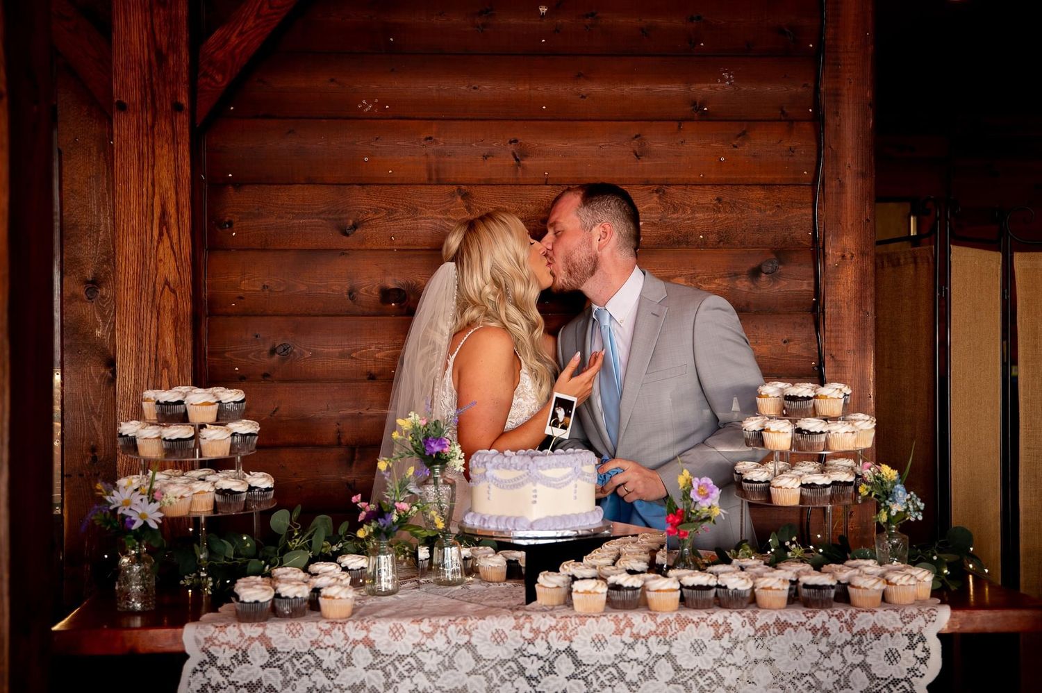 Couple sharing a moment at their rustic wedding dessert display with cupcakes and cake.