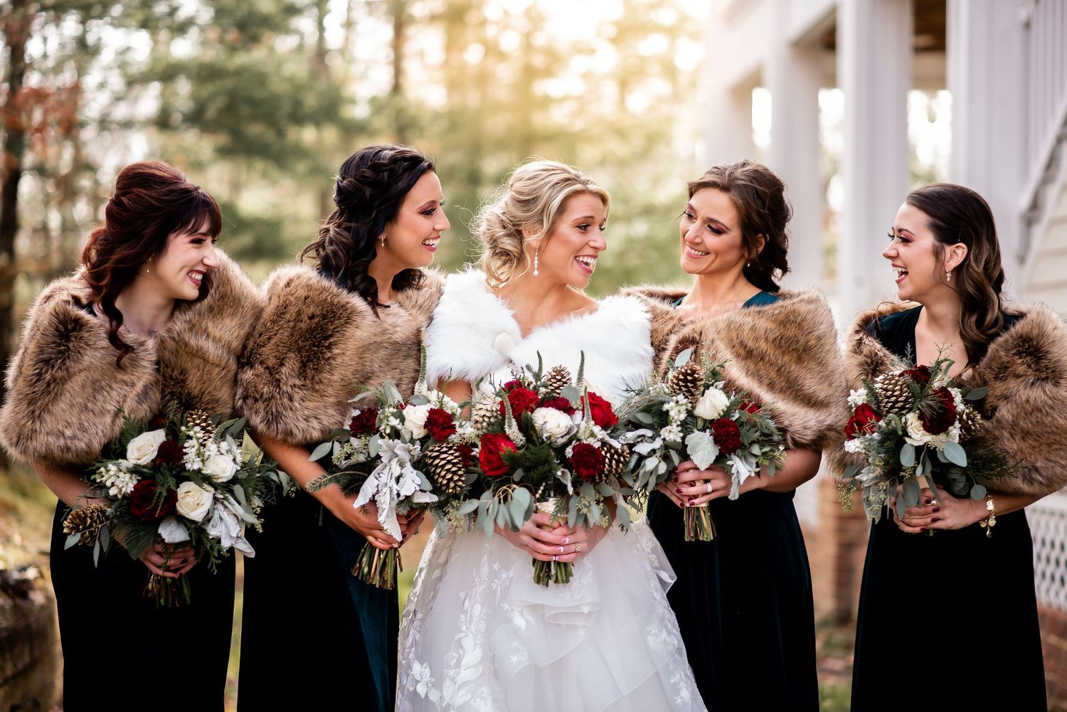 Bridesmaids in dark dresses pose with winter fur stoles and floral bouquets.