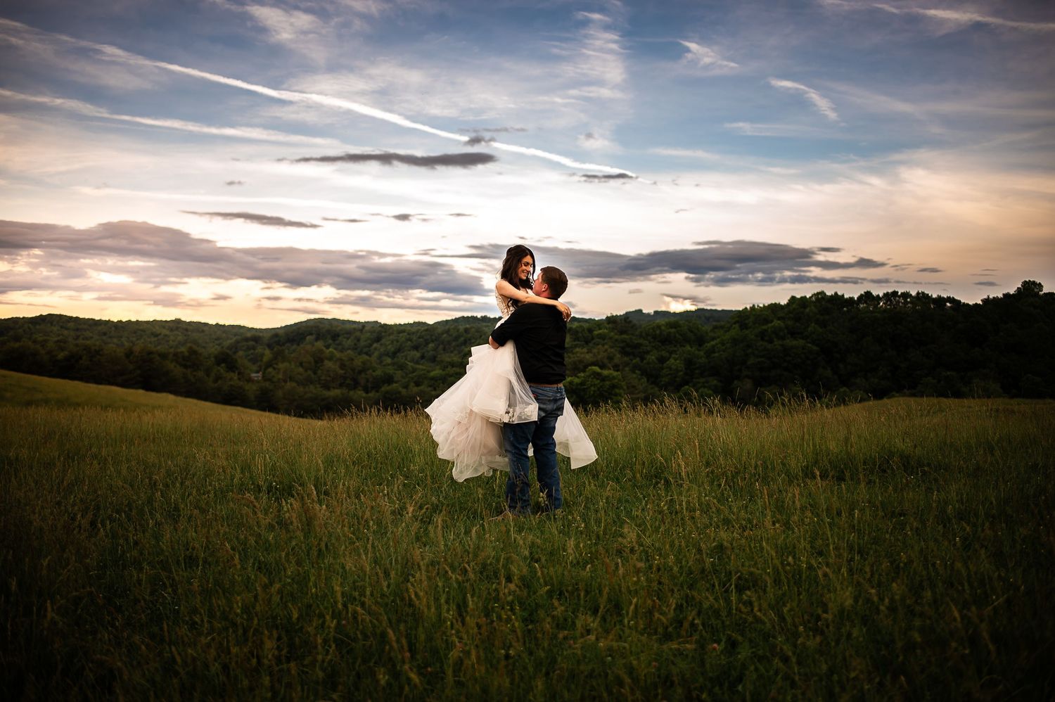 Silhouette of a couple dancing in a sunset field with dramatic sky and rolling hills.