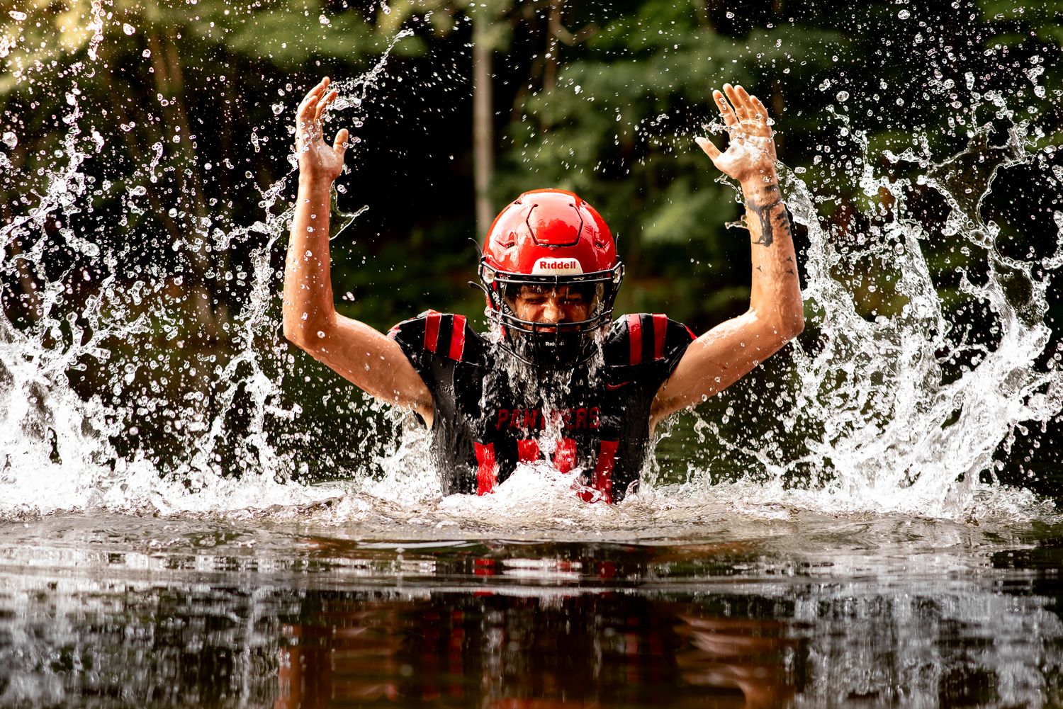 Dynamic water splash photo of athlete in red and black football uniform.