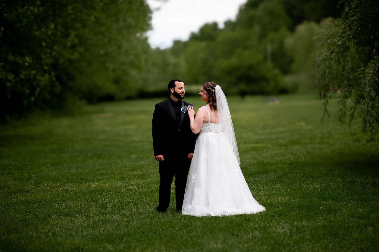 A couple shares an intimate moment during their wedding on a grassy hillside.