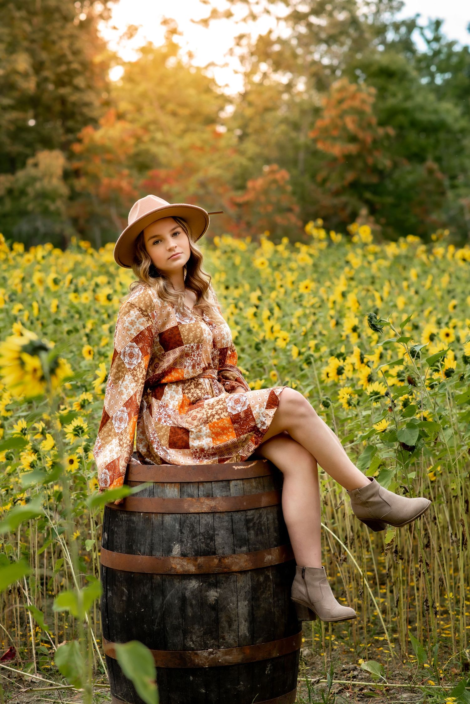 A rustic autumn scene with someone sitting on a wooden barrel in a field of yellow wildflowers at sunset.