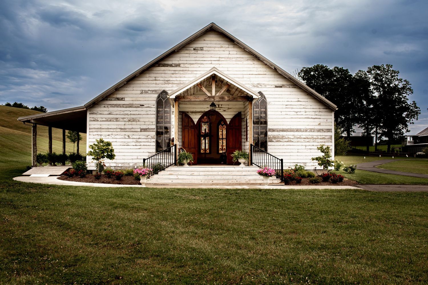 Rustic white church building photographed in panoramic view against cloudy sky.
