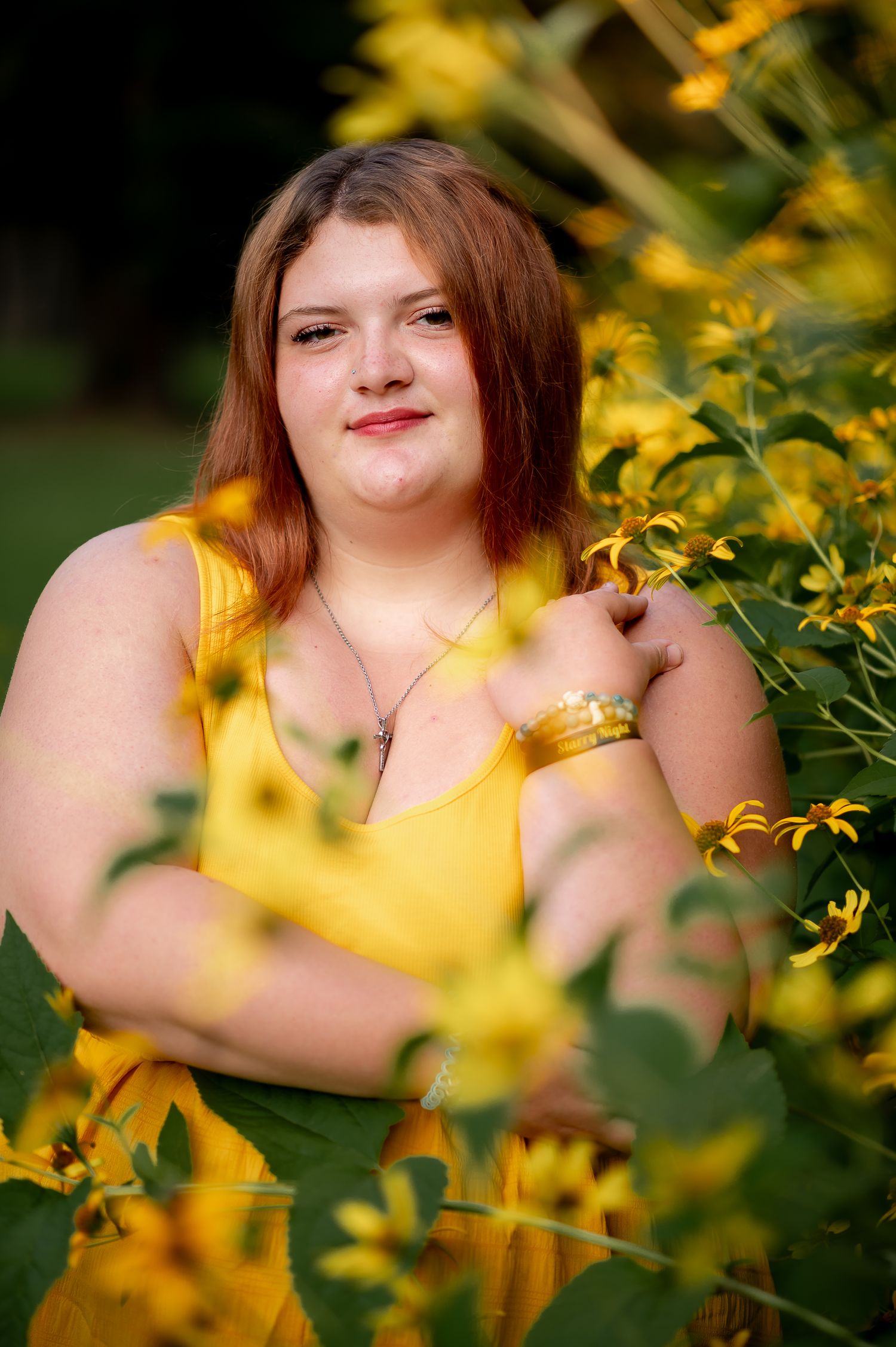 A person in a yellow top poses among blooming yellow flowers in a garden setting.