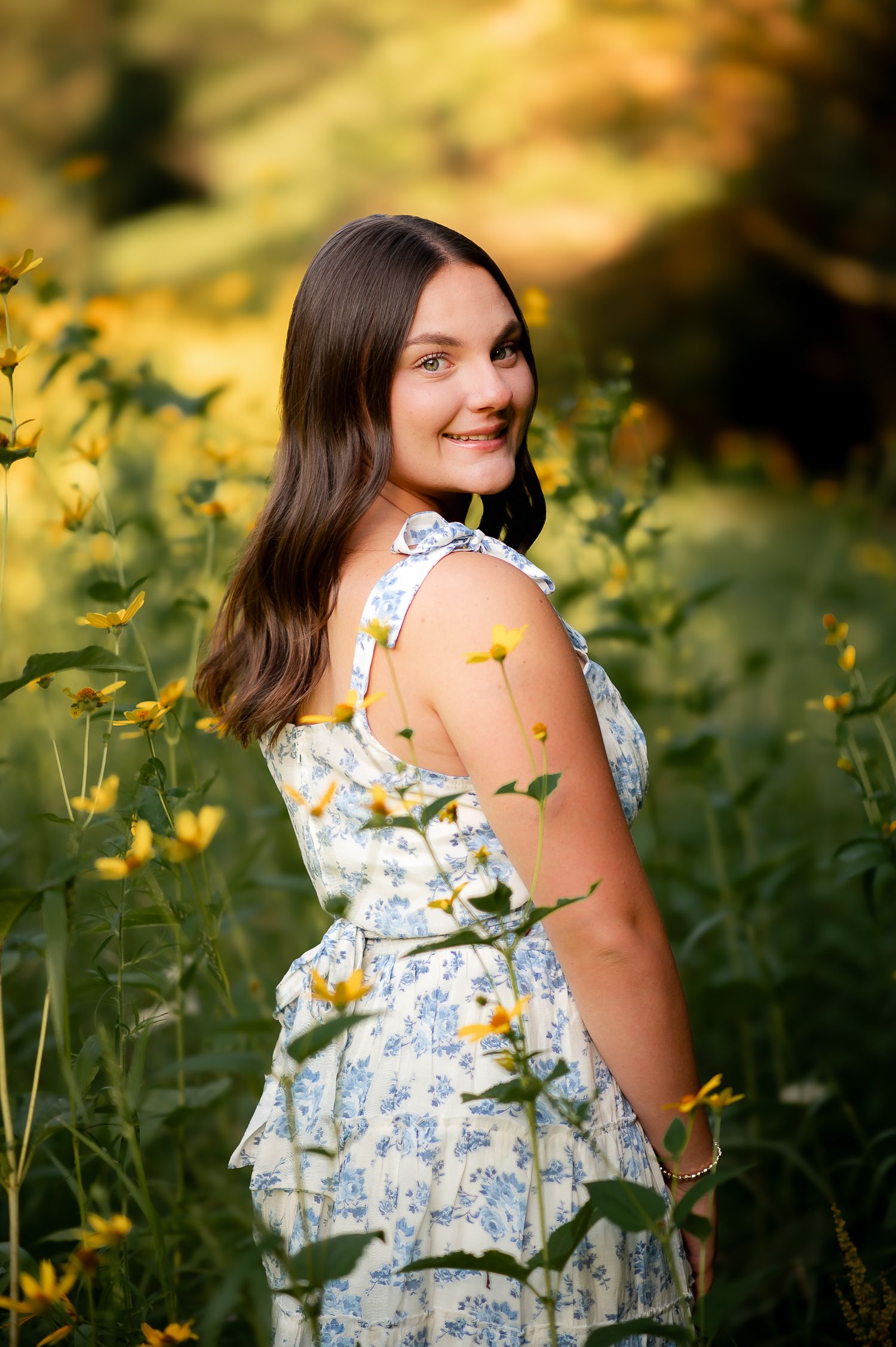 A summer portrait in a blue and white floral dress standing among yellow wildflowers during golden hour.