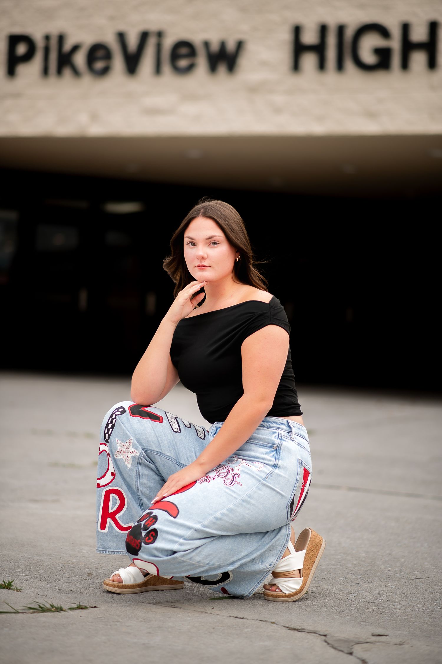 Senior portrait outside PikeView High School shows casual pose in ripped jeans and black top.