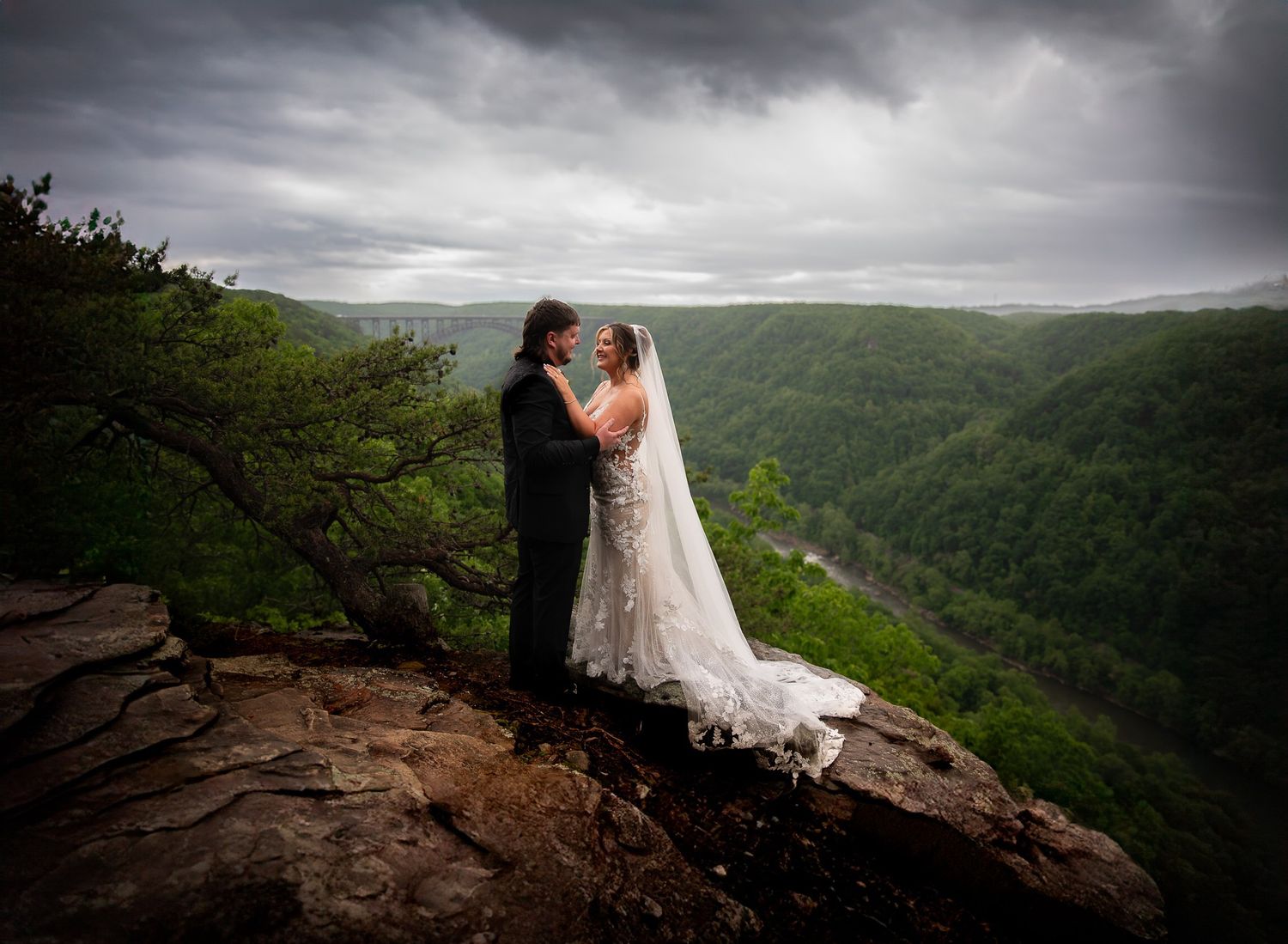 Dramatic wedding portrait on rocky cliff overlooking misty mountain valley.