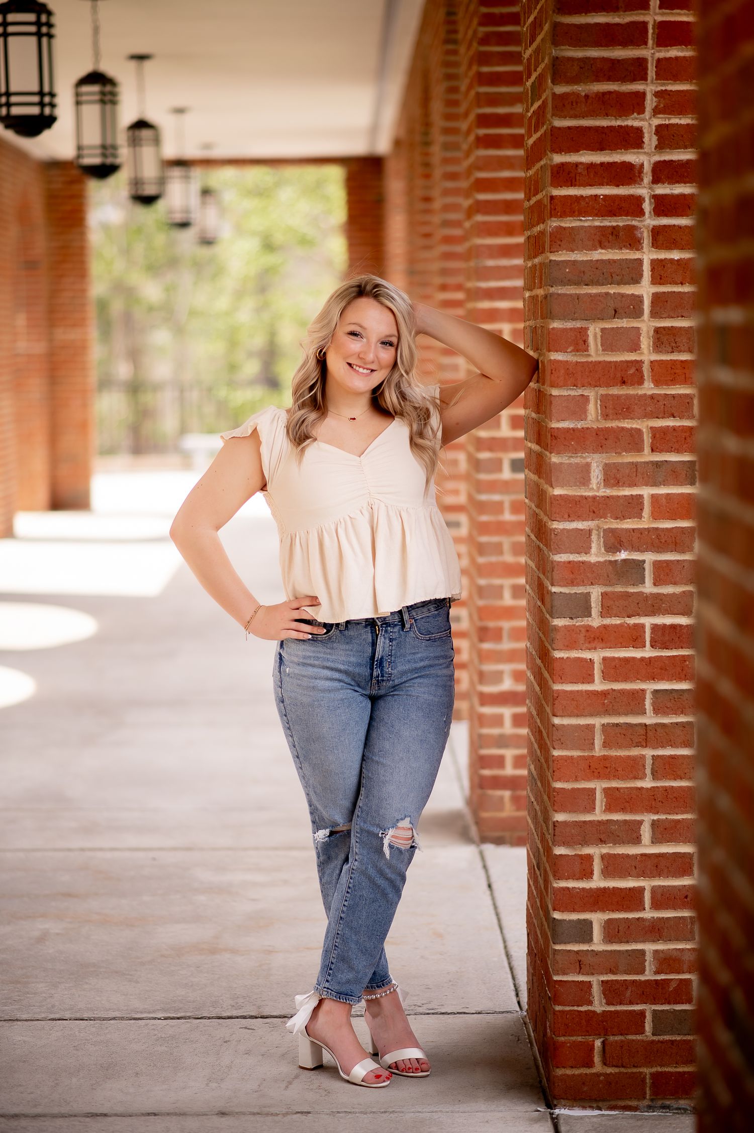 A casual portrait in a white top and distressed jeans posing in a brick colonnade with pendant lights.