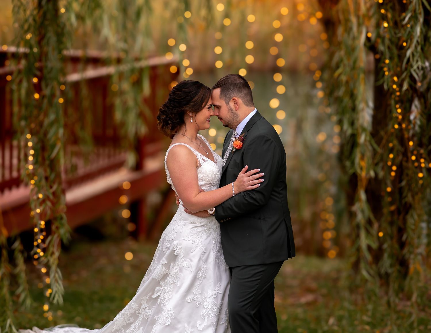 Couple sharing intimate moment during outdoor wedding ceremony with string lights and greenery.